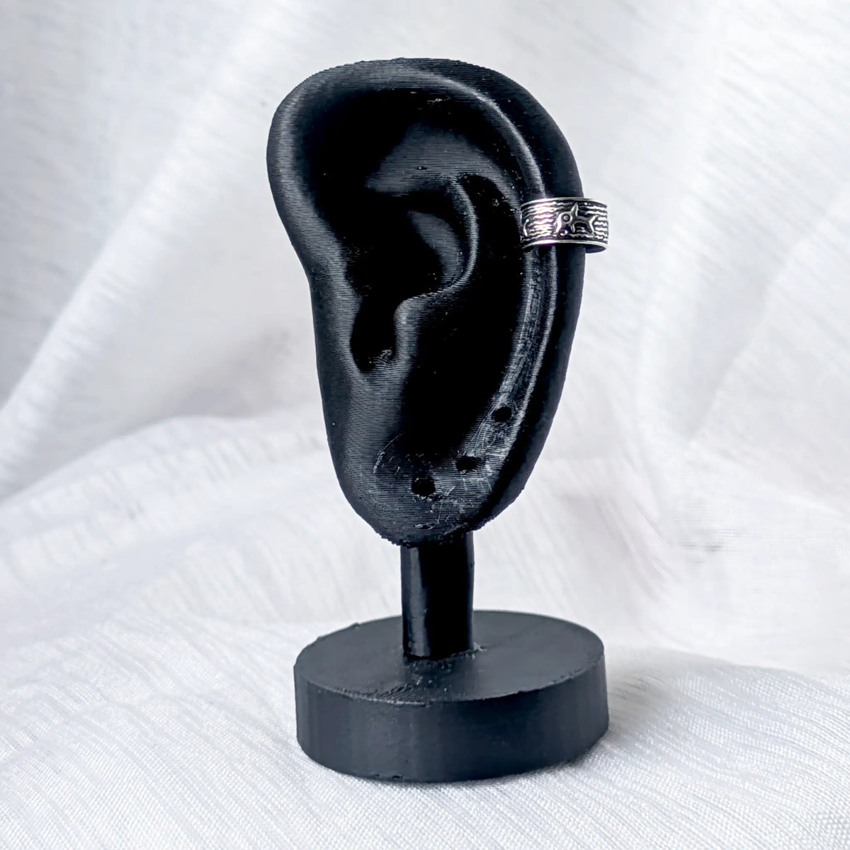 Silberner Ear Cuff im maritimen Design, festgeklemmt am oberen Knorpel eines schwarzen 3D-Ohr-Displays.