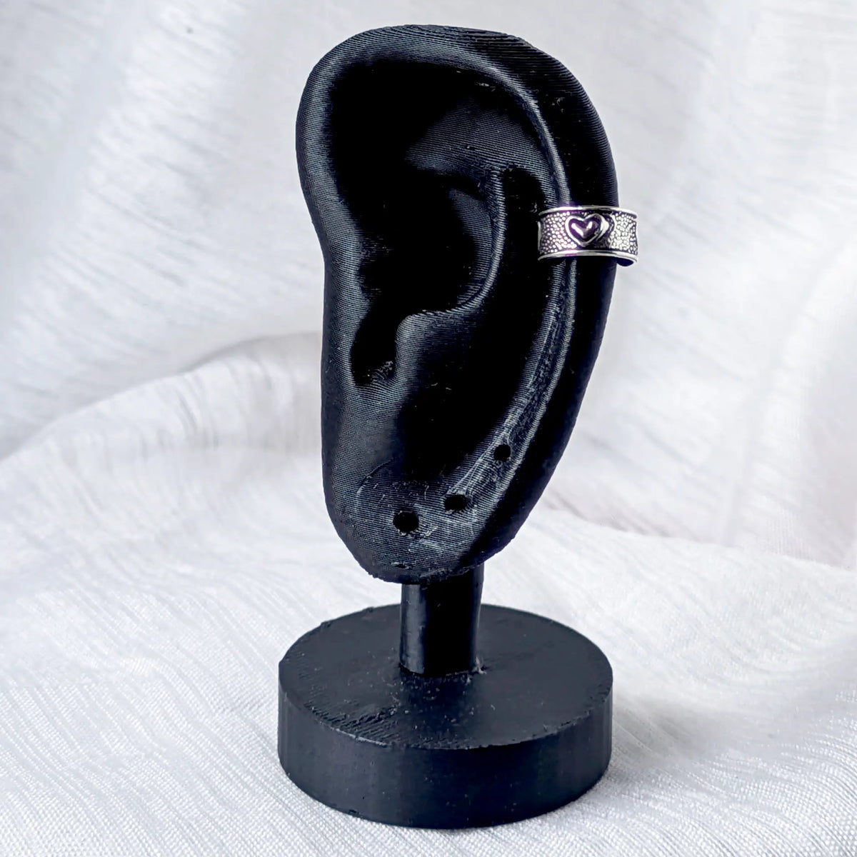 Silberner Herz Ear Cuff im Tragebeispiel an einem schwarzen Ohr-Display fixiert.