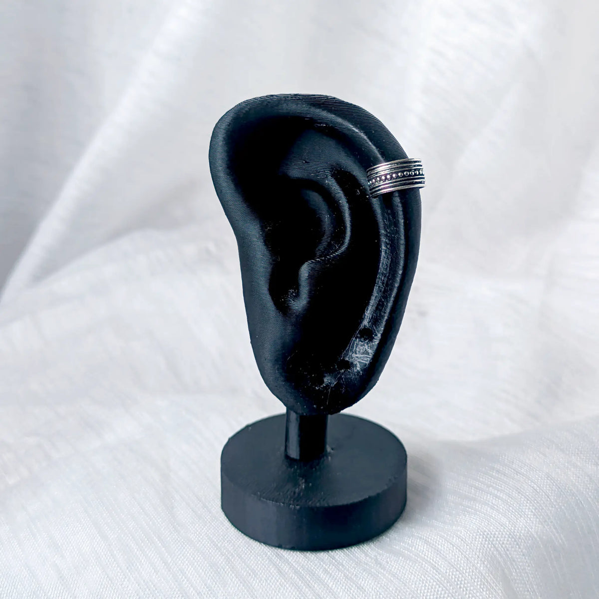 Silberner Ear Cuff im Kugel-Design, getragen am äußeren Knorpel eines schwarzen 3D-Ohr-Displays.
