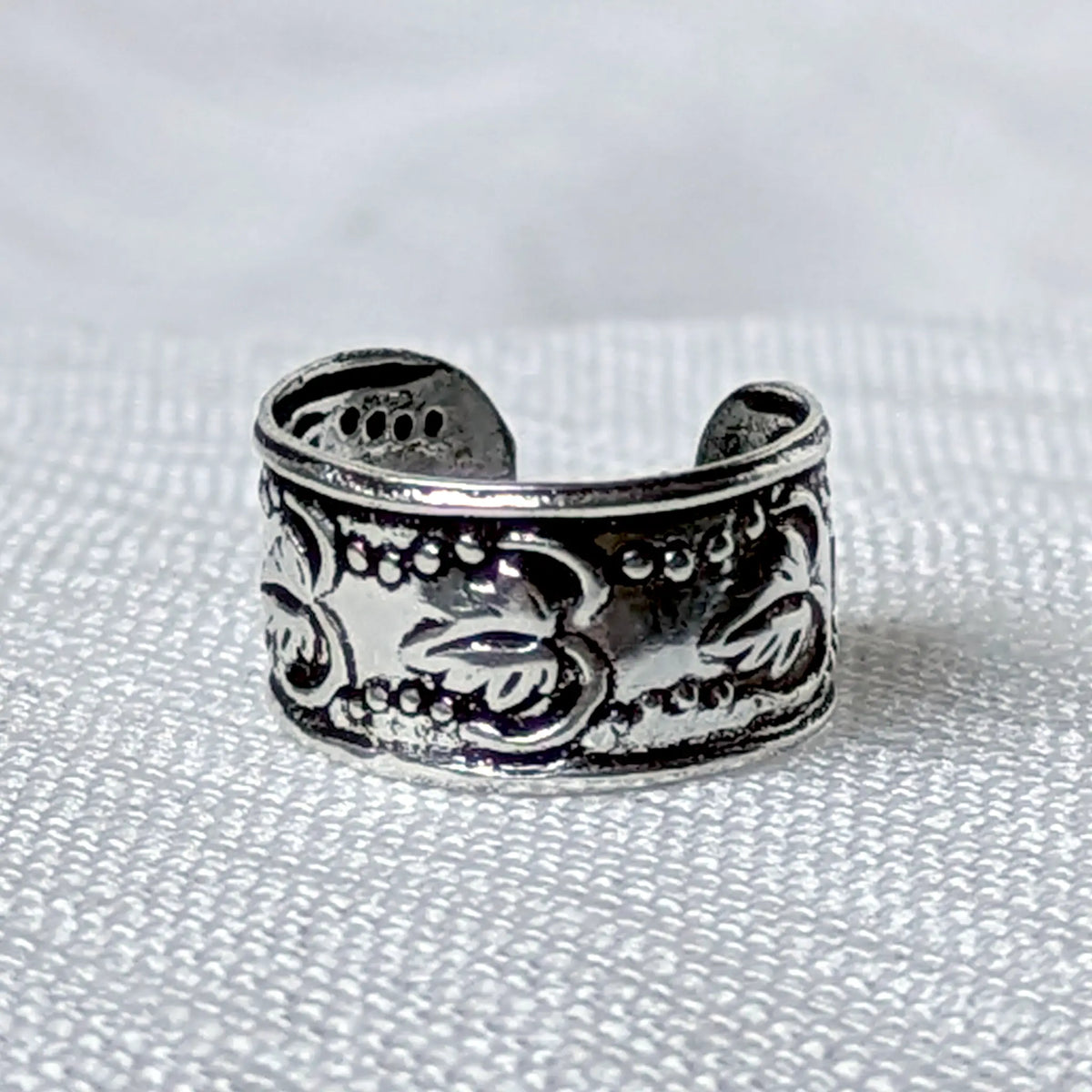 Nahaufnahme einer breiten Ohrklemme aus 925 Silber mit geprägtem Vintage Blätter- und Rankenmuster auf geschwärztem Grund.