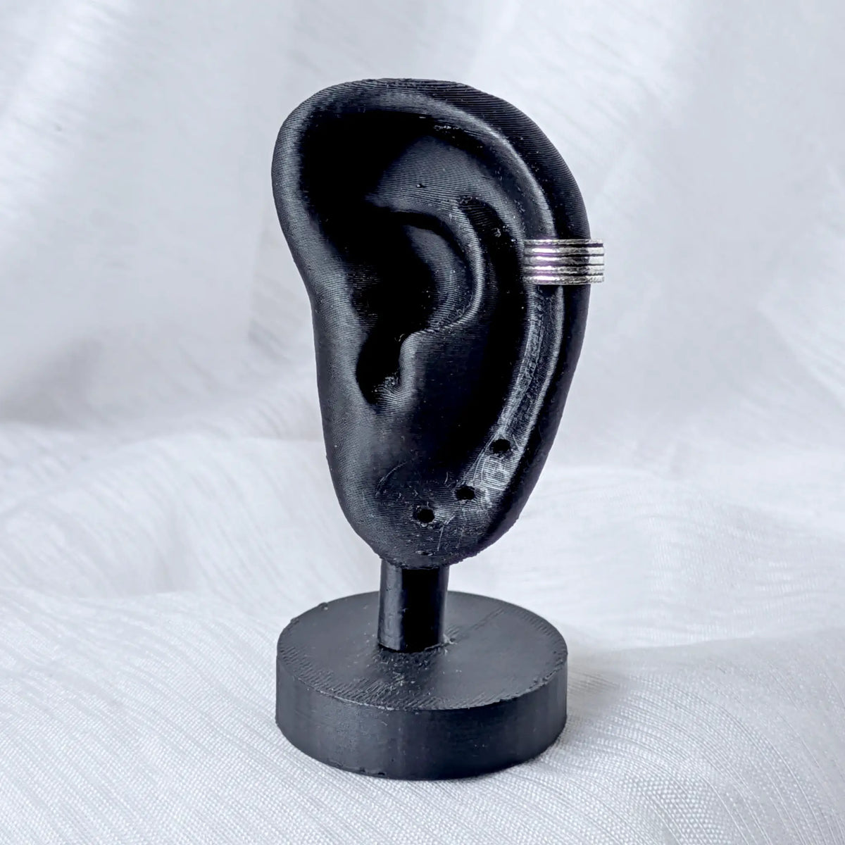 Mehrreihiger Silber Ear Cuff, getragen am äußeren Knorpel eines schwarzen 3D-Ohr-Displays.