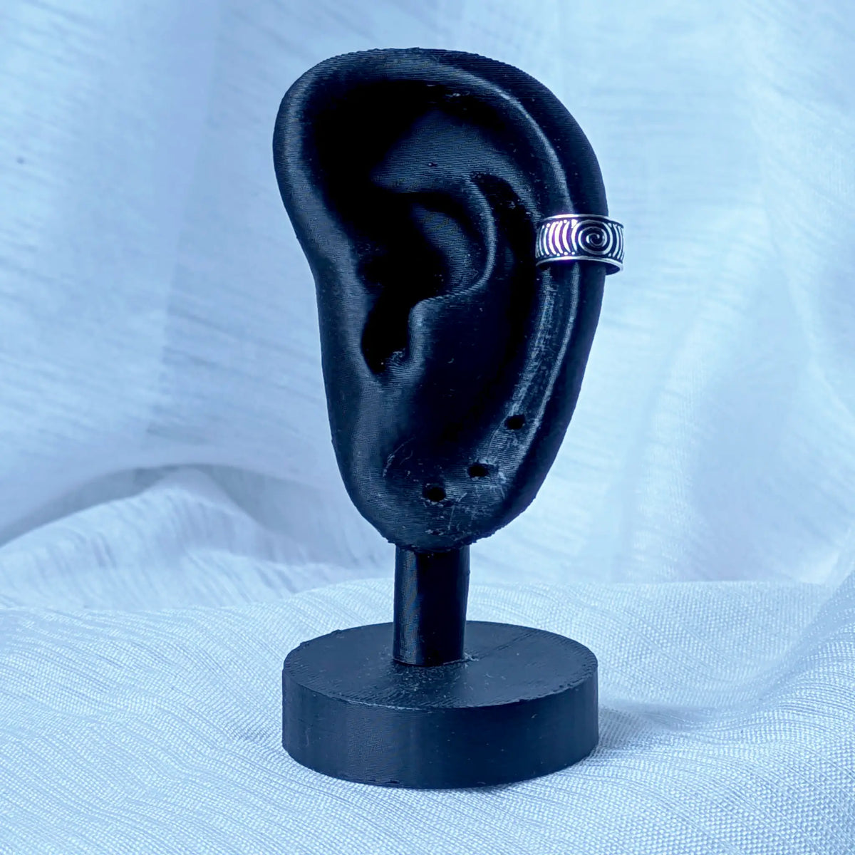 Die oxidierte Silber-Ohrklemme mit Spiral-Muster ist stilvoll an der Knorpelkante eines schwarzen 3D-Ohr-Displays platziert.
