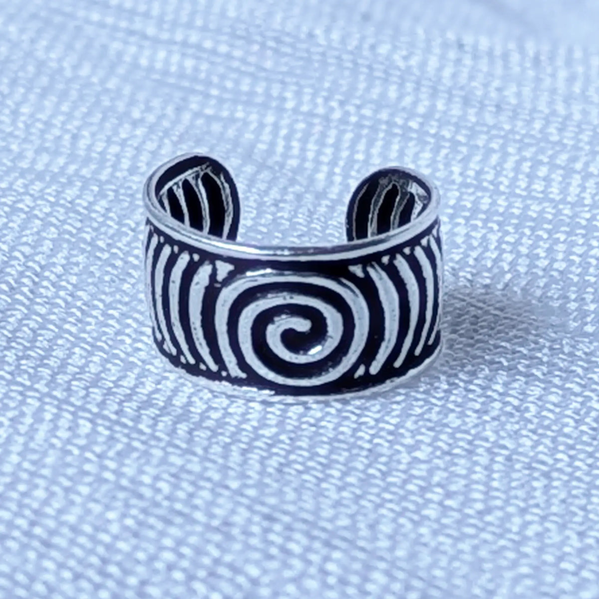 Nahaufnahme eines breiten Silber Ear Cuffs, die das plastische Spiral-Muster und die oxidierten, schwarzen Zwischenräume im Detail zeigt.
