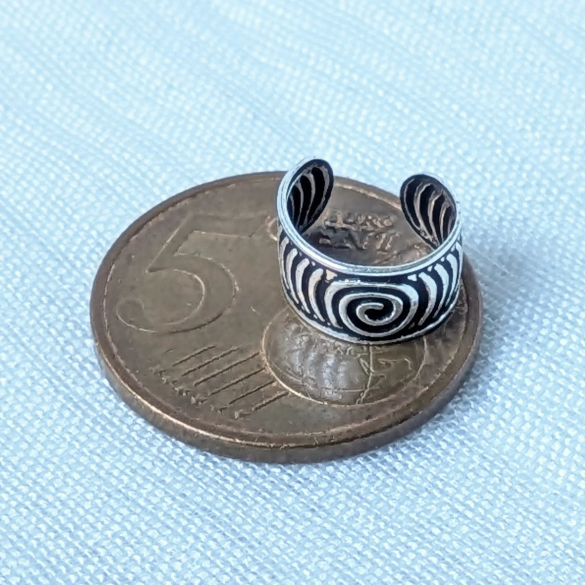 Der Tribal Ear Cuff mit Spiralmuster liegt zum visuellen Größenvergleich neben einer 5-Cent-Münze, um die kompakte Passform zu demonstrieren.
