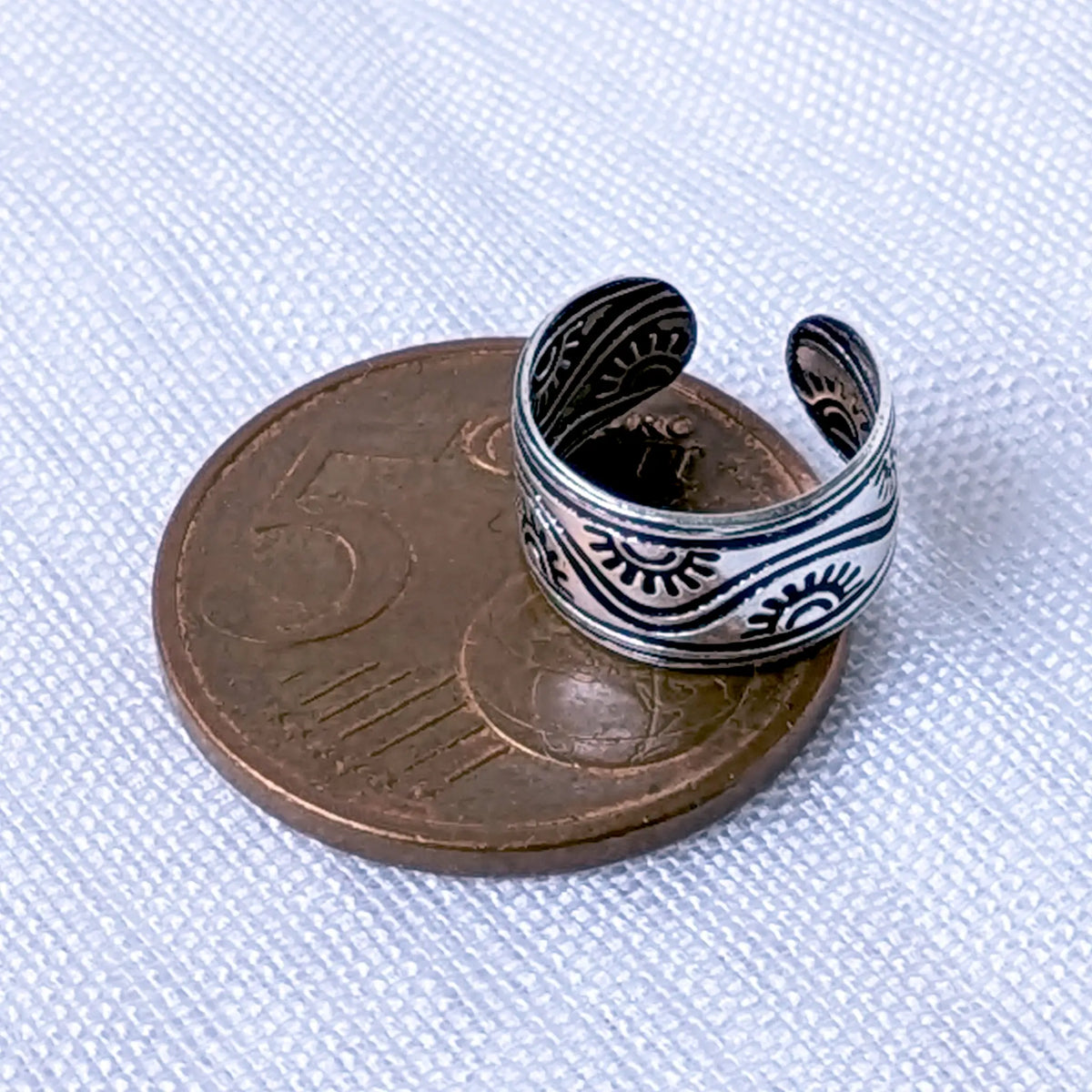 Größenvergleich: Die breite 925 Silber Ohrklemme mit dem Sonnen- und Wellen-Motiv liegt flach auf einer 5-Cent-Münze.
