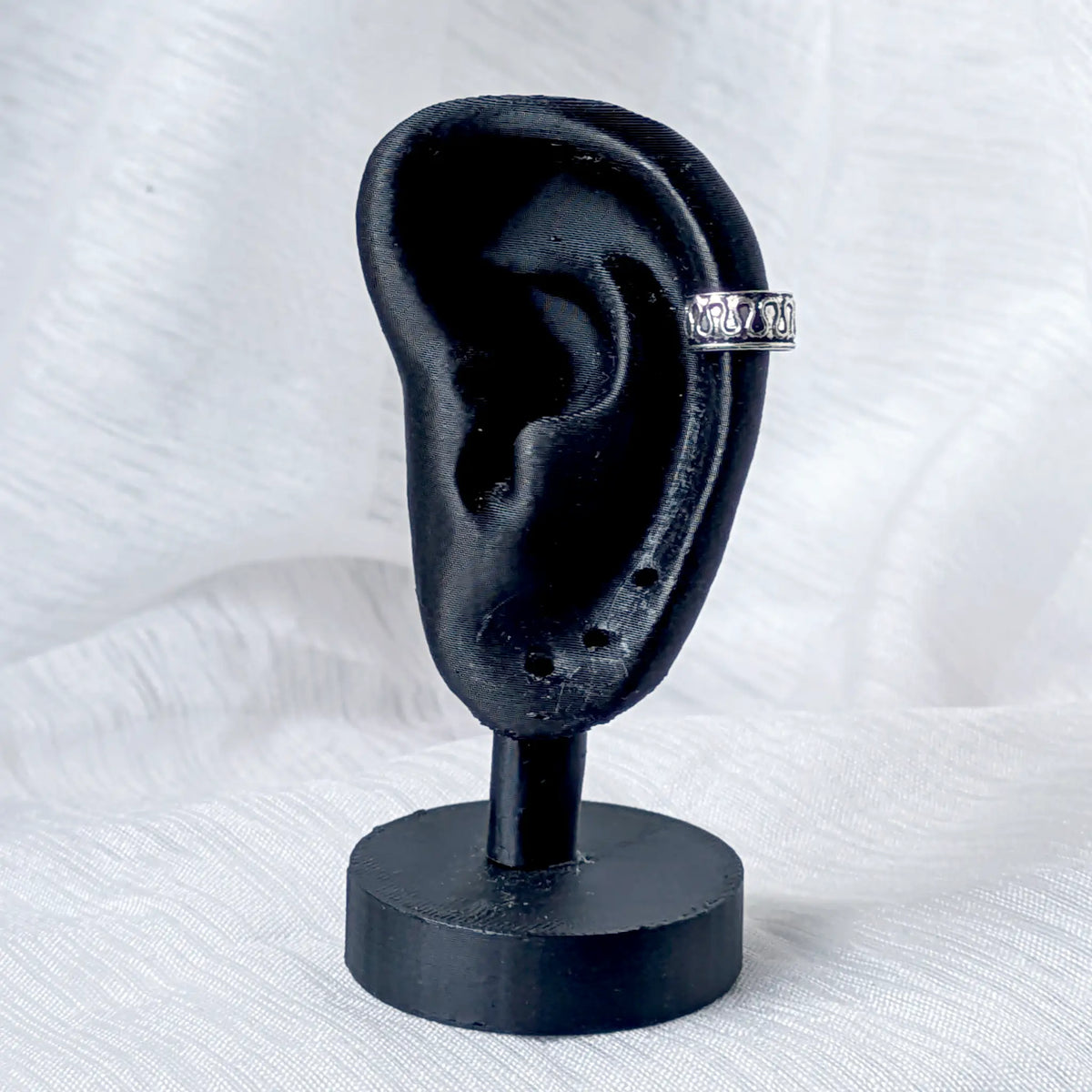 Tragebeispiel des silbernen Ear Cuffs mit Wellen-Muster, fixiert am seitlichen Knorpel eines schwarzen Ohr-Displays.
