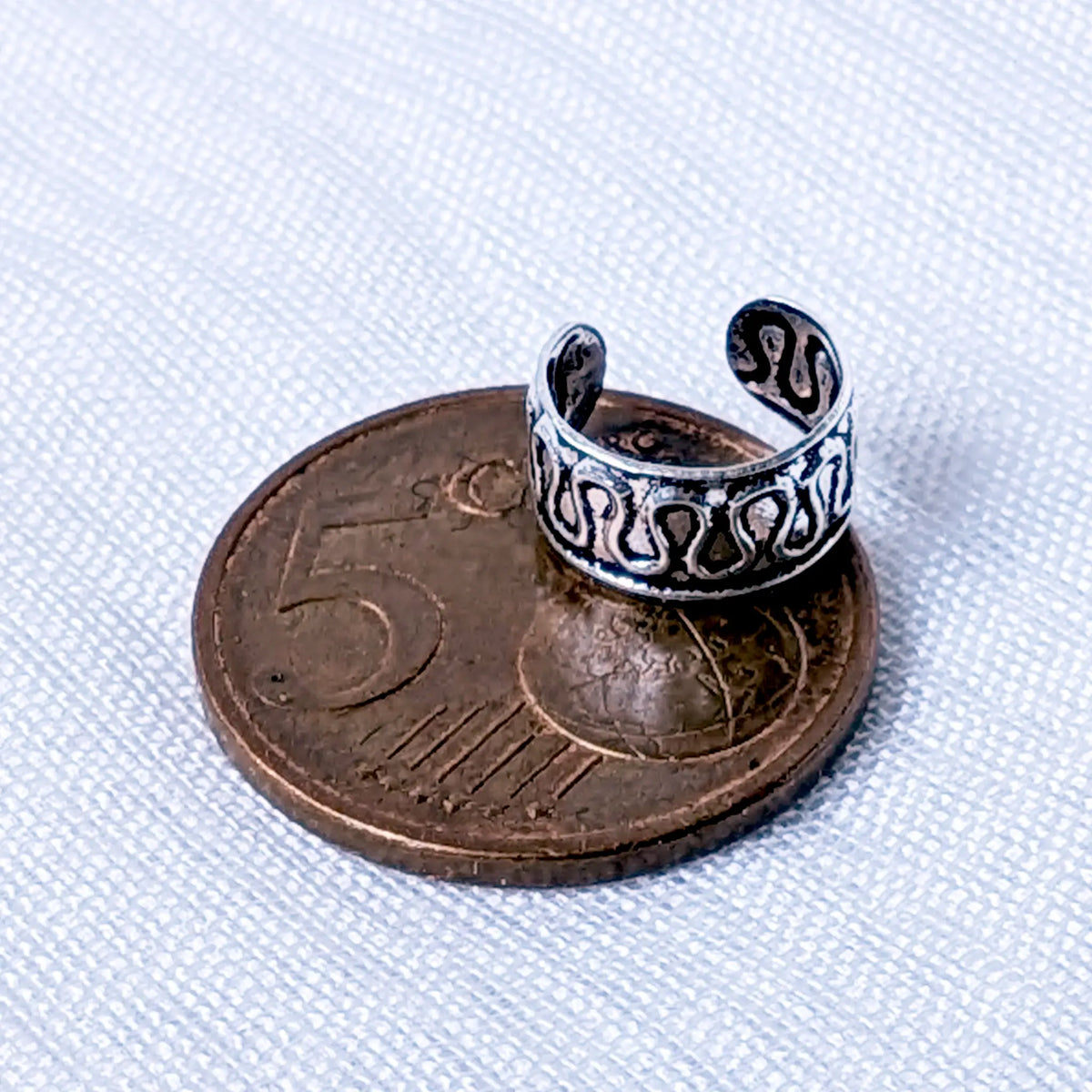 Größenvergleich: Die silberne Ohrklemme mit Cut-Out-Design liegt zur Veranschaulichung der Proportionen auf einer 5-Cent-Münze.
