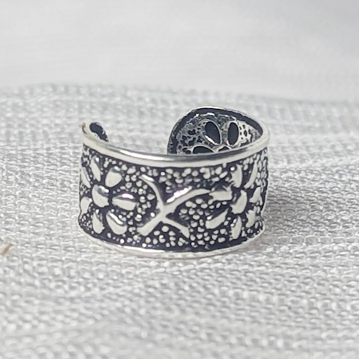 Nahaufnahme einer 925 Silber Ohrklemme mit floralem Blumenmuster und fein gepunktetem Hintergrund.