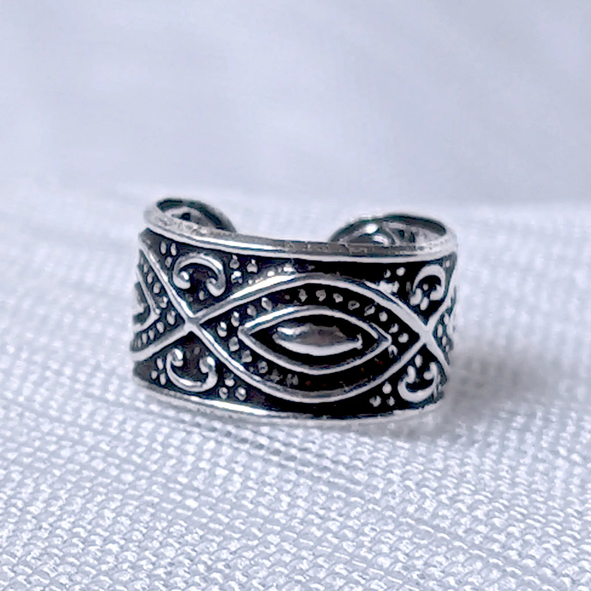 Nahaufnahme einer breiten Ohrklemme aus 925 Silber mit stilisiertem Augen-Motiv und ornamentalen Verzierungen auf geschwärztem Grund.