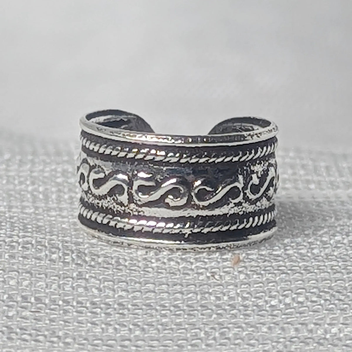 Nahaufnahme einer breiten Ohrklemme aus 925 Silber mit S-Wellenmuster und Kordelrand auf geschwärztem Grund.