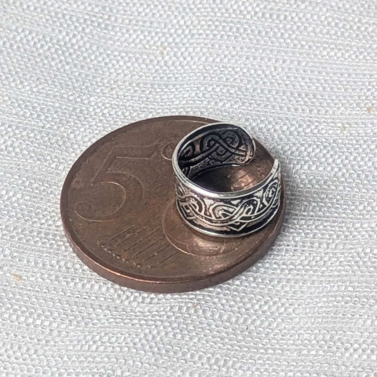 Größenvergleich: Die silberne Ohrklemme mit Wellenmuster liegt auf einer 5-Cent-Münze, um die kompakten Maße zu verdeutlichen.