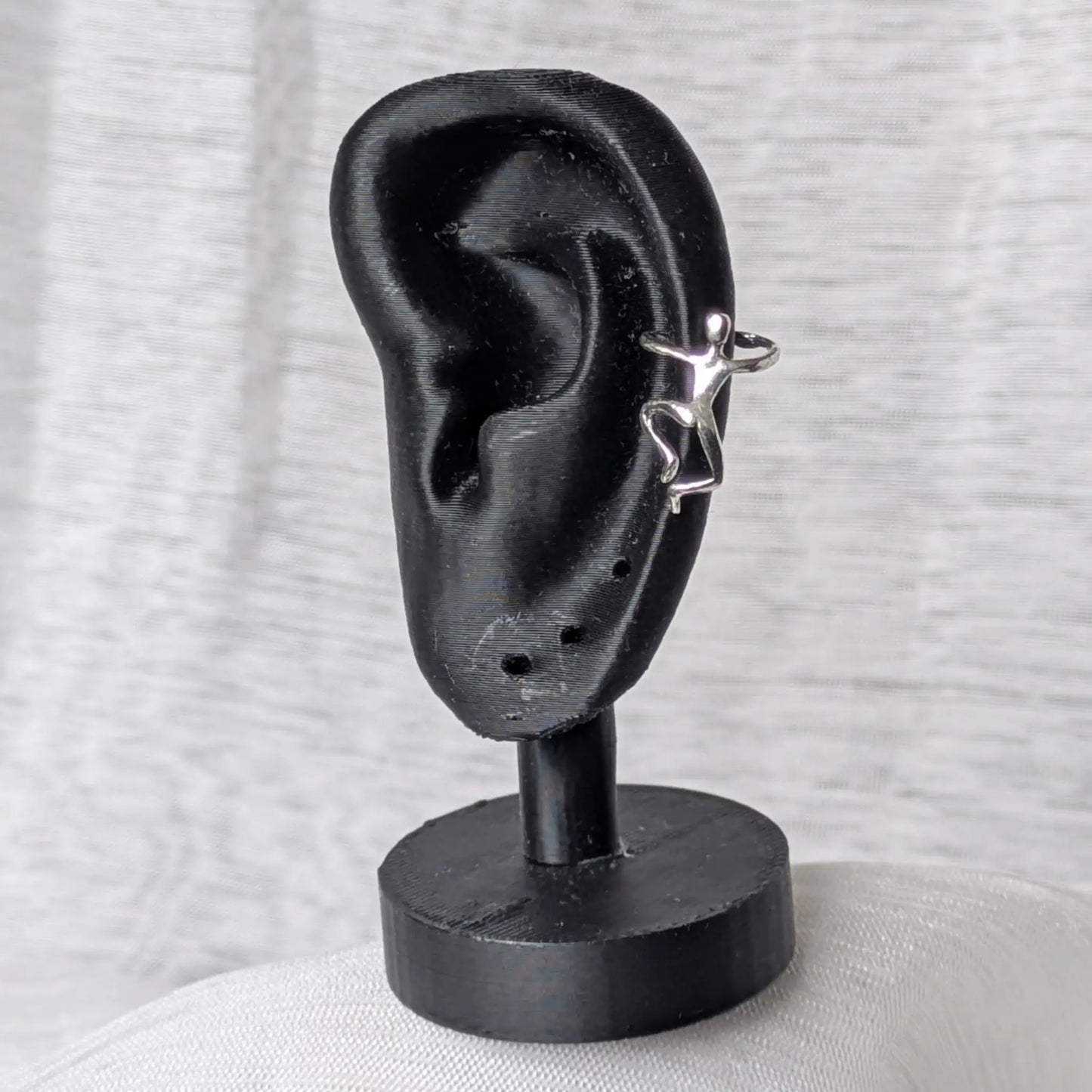 Der 925 Silber Earcuff mit der kletternden Figur, getragen am Rand eines schwarzen Ohr-Displays.