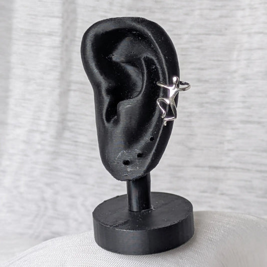 Der 925 Silber Earcuff mit der kletternden Figur, getragen am Rand eines schwarzen Ohr-Displays.