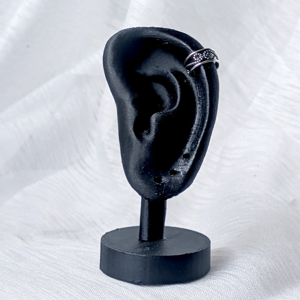 Filigrane Silber-Ohrklemme mit Knoten-Muster, stilvoll getragen am äußeren Helix-Knorpel eines schwarzen 3D-Ohr-Displays.