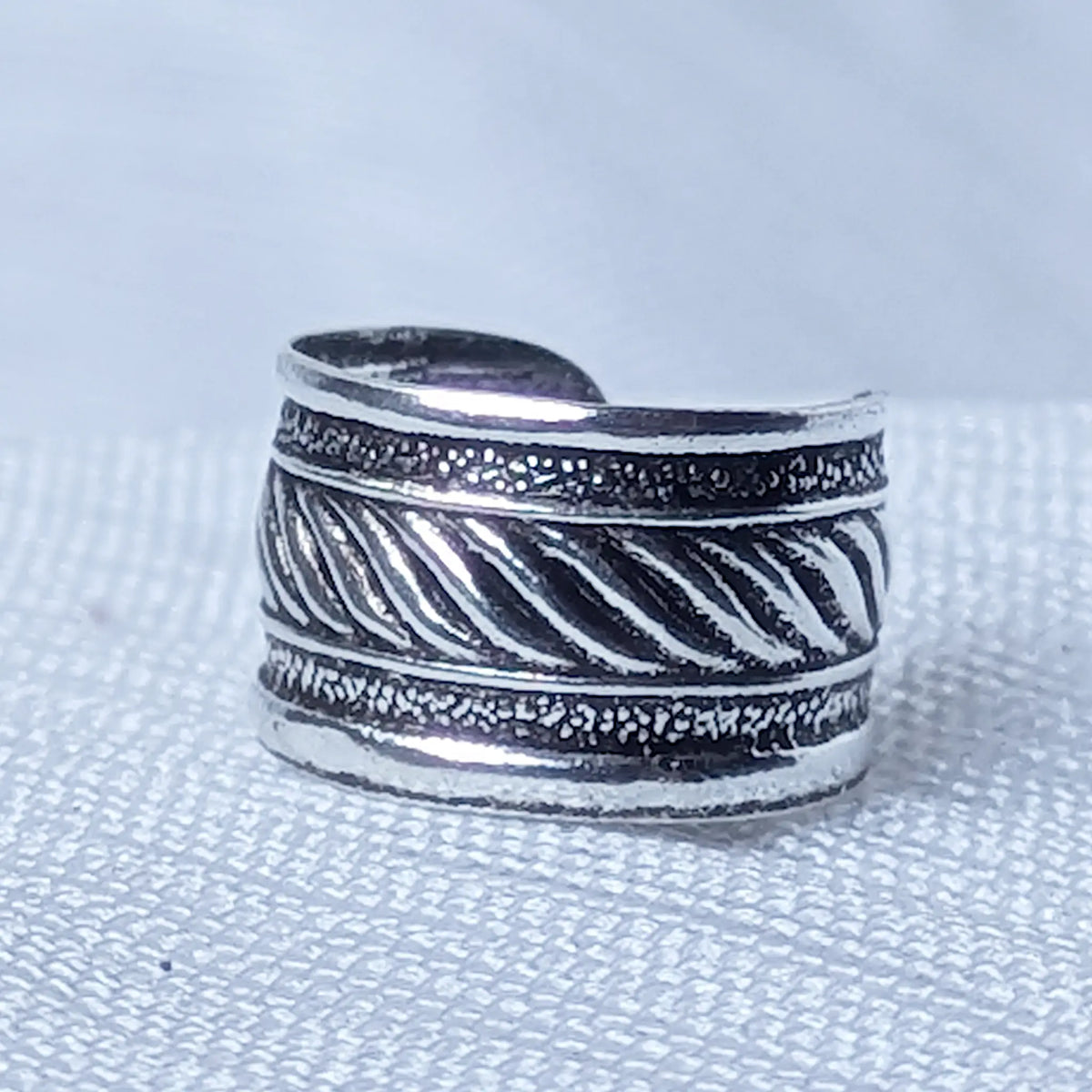 Nahaufnahme einer breiten Ohrklemme aus 925 Silber mit zentralem Kordelmuster und strukturierten Rändern auf geschwärztem Grund.