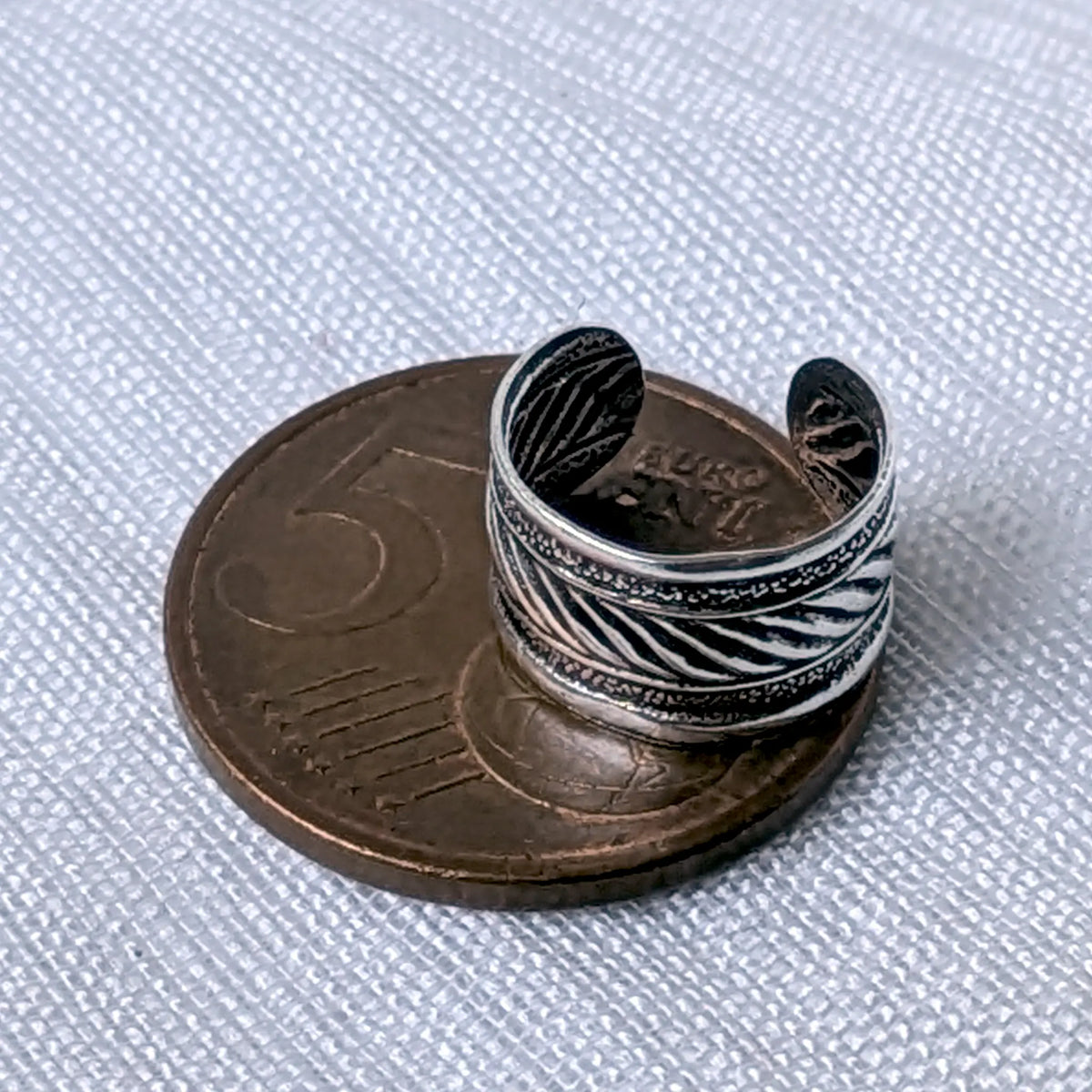 Größenvergleich der breiten, texturierten Silber-Ohrklemme mit Kordelmuster, zur Veranschaulichung auf einer 5-Cent-Münze platziert.