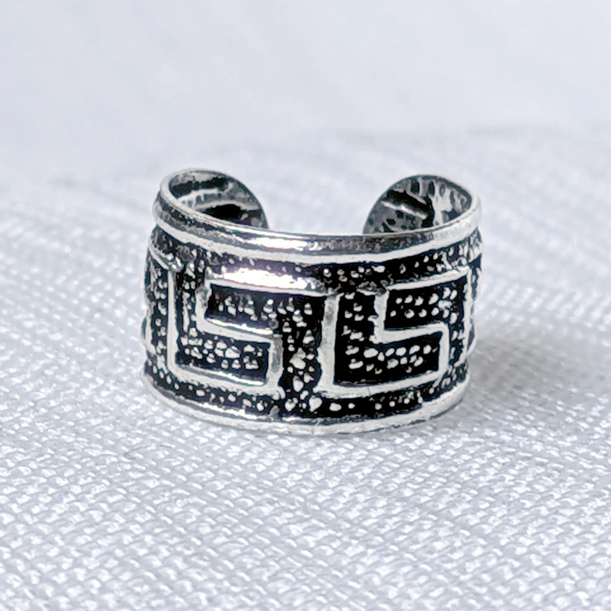 Nahaufnahme einer breiten Ohrklemme aus 925 Silber mit klassischem Mäander-Muster auf strukturiertem, geschwärztem Grund.