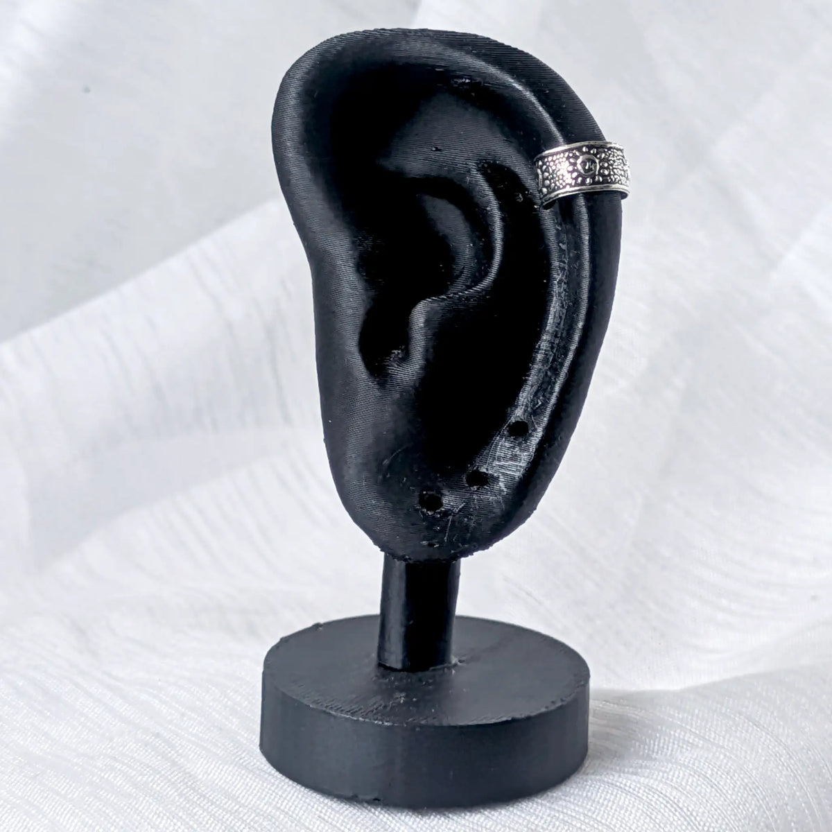 Silberne Ohrklemme mit mystischem Sonnen-Gesicht, stilvoll getragen am äußeren Helix-Knorpel eines schwarzen 3D-Ohr-Displays.
