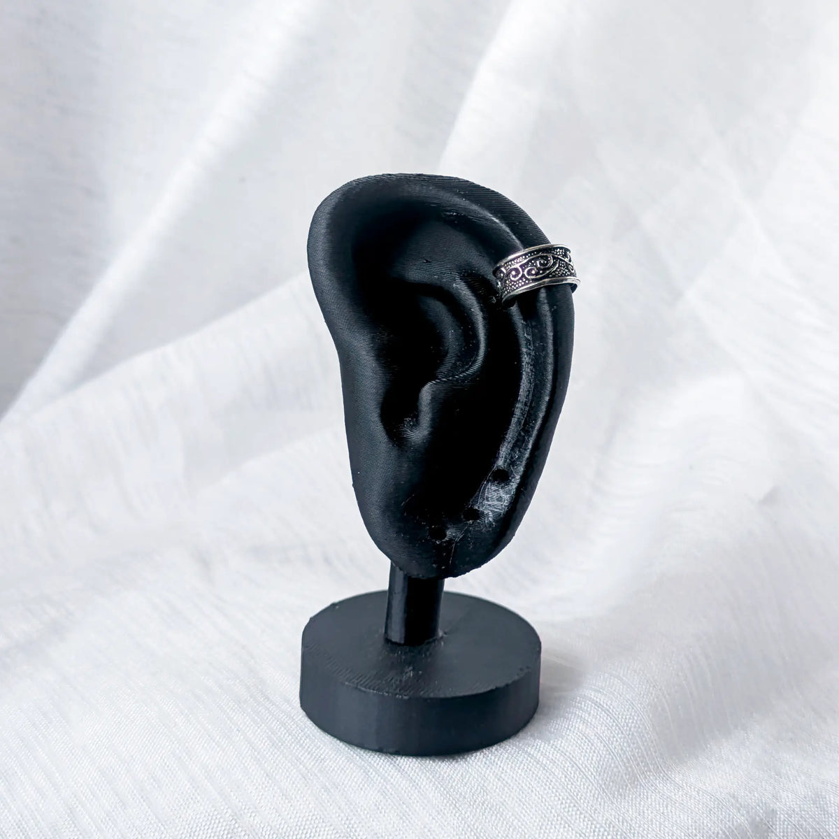 Silberne Ohrklemme mit Schnörkel-Design, stilvoll getragen am äußeren Helix-Knorpel eines schwarzen 3D-Ohr-Displays.