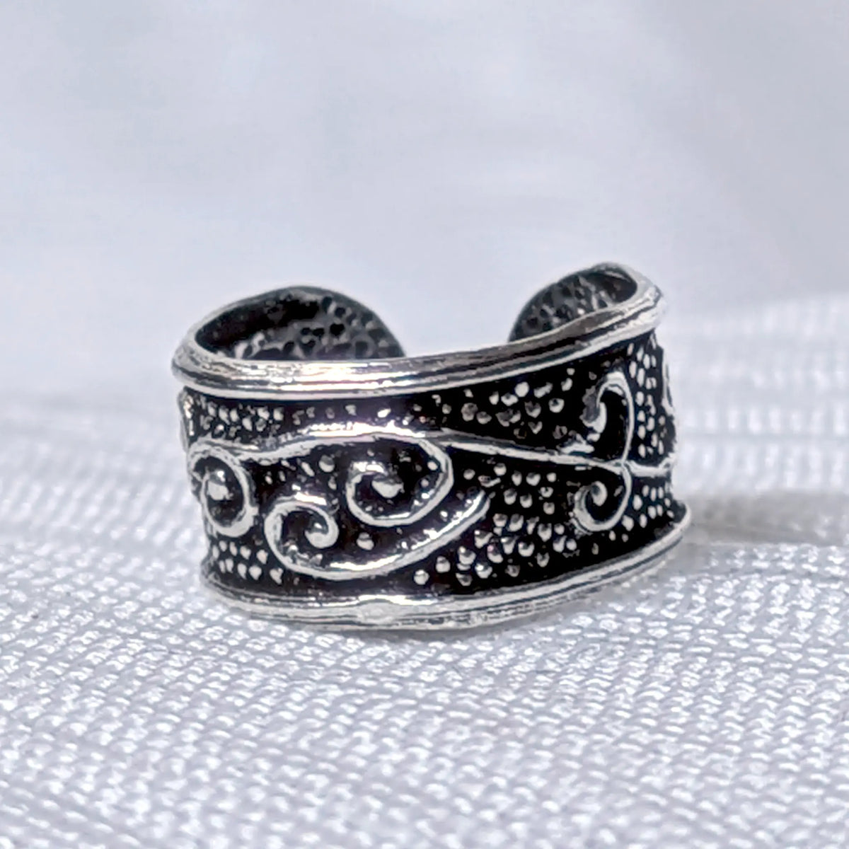 Nahaufnahme einer breiten Ohrklemme aus 925 Silber mit erhabenen Schnörkel-Ornamenten auf strukturiertem, geschwärztem Grund.