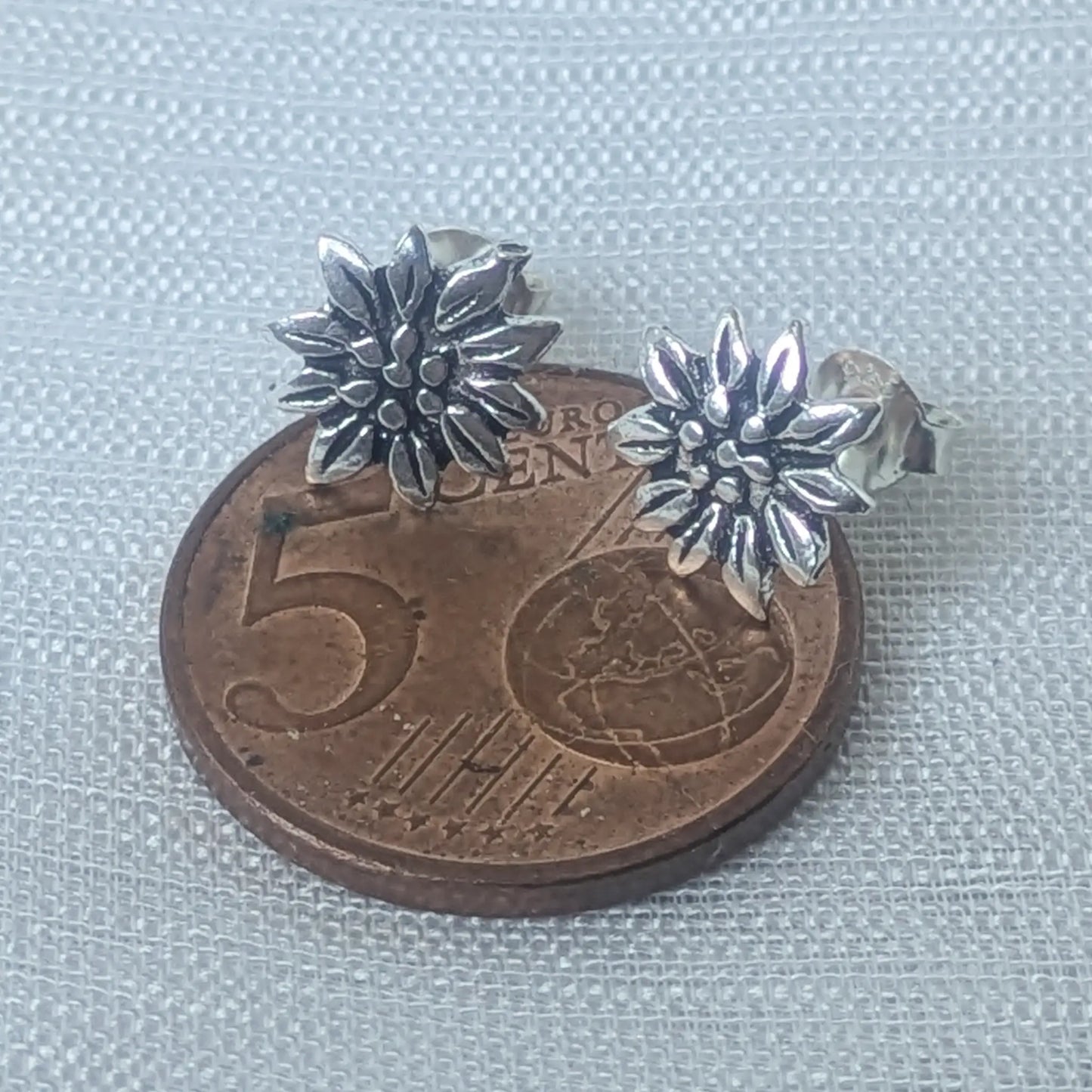 Größenvergleich der filigranen Edelweiß Silber-Ohrstecker platziert auf einer 5-Cent-Münze.