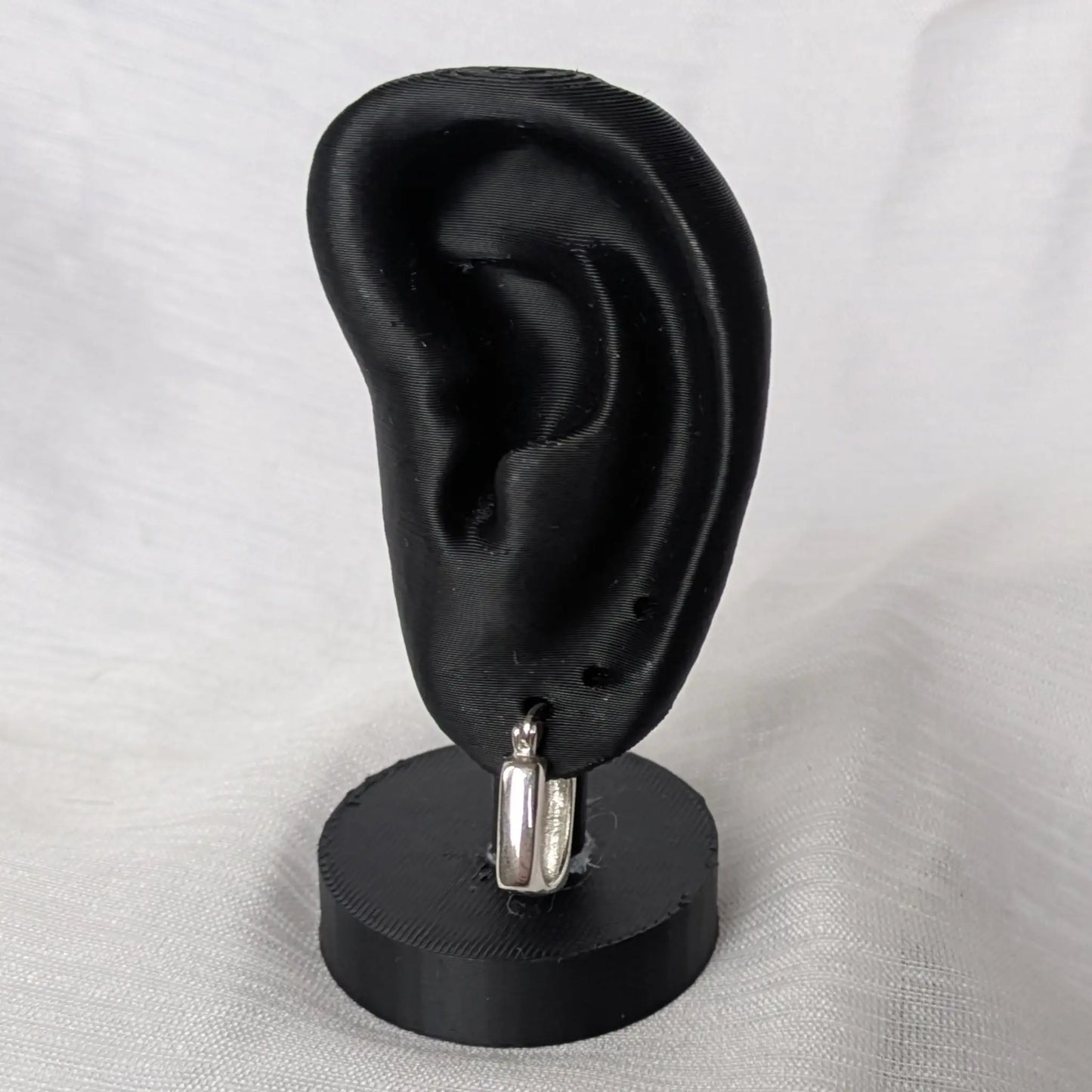 Quadratische Silber-Creolen elegant präsentiert auf einem schwarzen Ohr-Display.