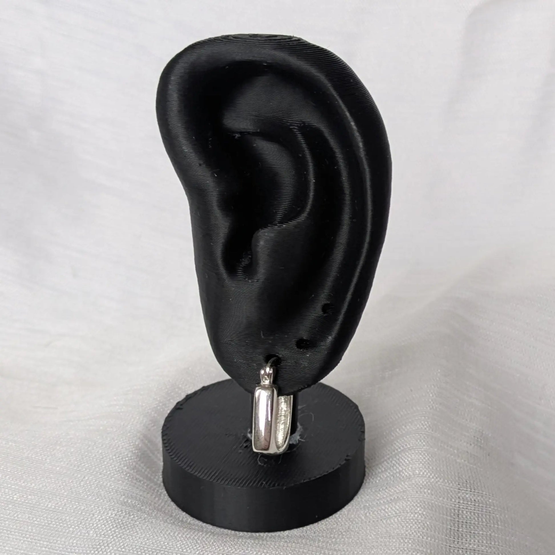 Quadratische Silber-Creolen elegant präsentiert auf einem schwarzen Ohr-Display.