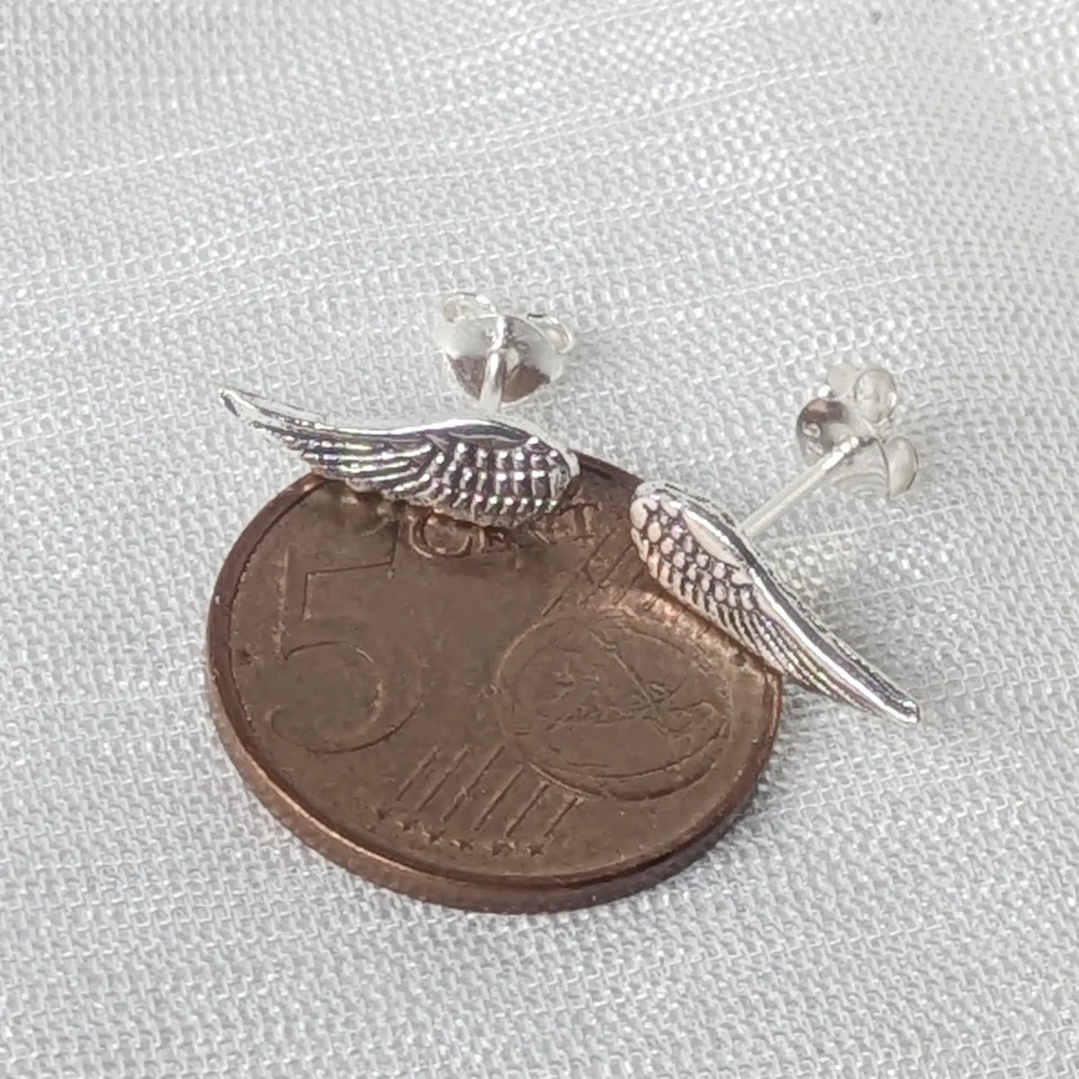 Kleine Engelsflügel Ohrstecker aus 925 Silber liegend auf einer 5-Cent-Münze zum genauen Größenvergleich.
