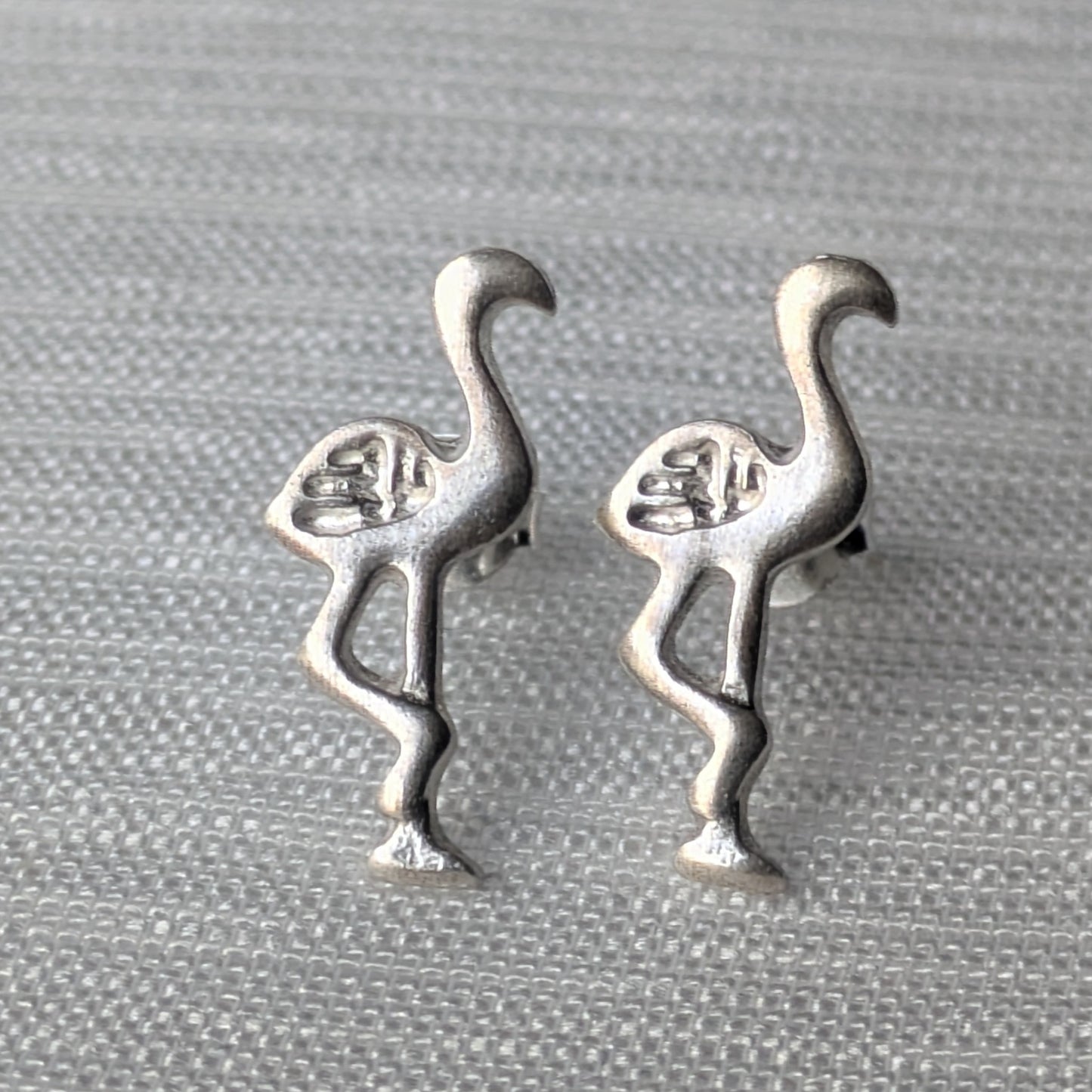 Paar Flamingo Ohrstecker aus mattem 925 Sterling Silber in charakteristischer Einbein-Pose auf hellem Hintergrund.