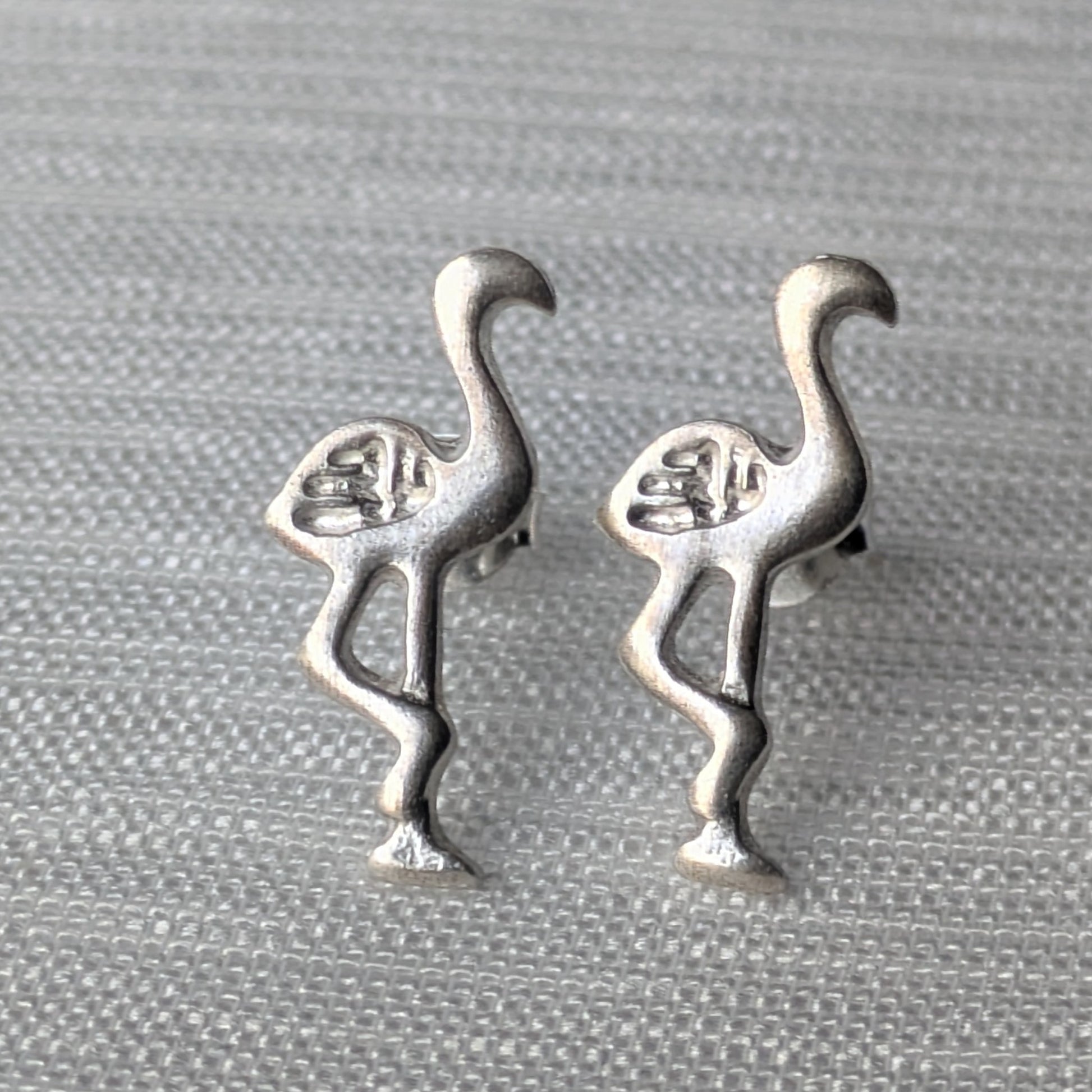 Paar Flamingo Ohrstecker aus mattem 925 Sterling Silber in charakteristischer Einbein-Pose auf hellem Hintergrund.