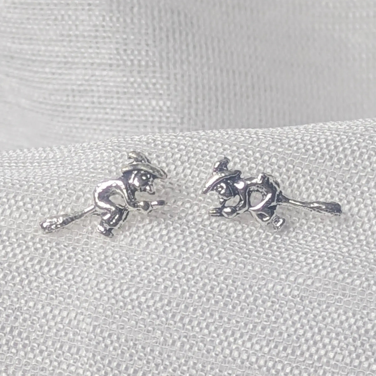 Detailaufnahme von 925 Silber Ohrsteckern im Motiv fliegende Hexe auf Besen mit Spitzhut.
