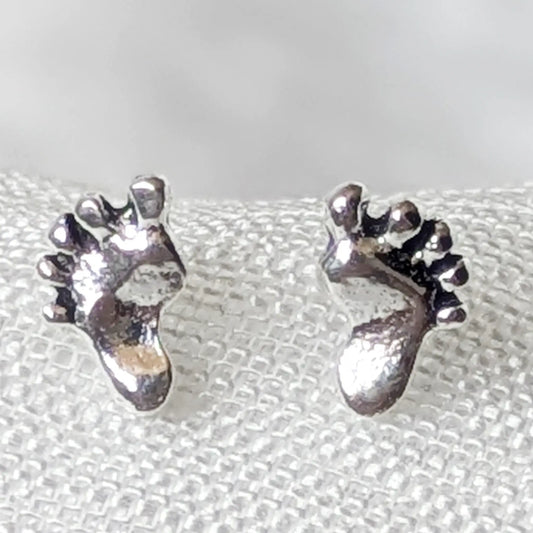 Nahaufnahme von zwei detailreichen Ohrsteckern in Form von Babyfüßen aus 925er Sterlingsilber.