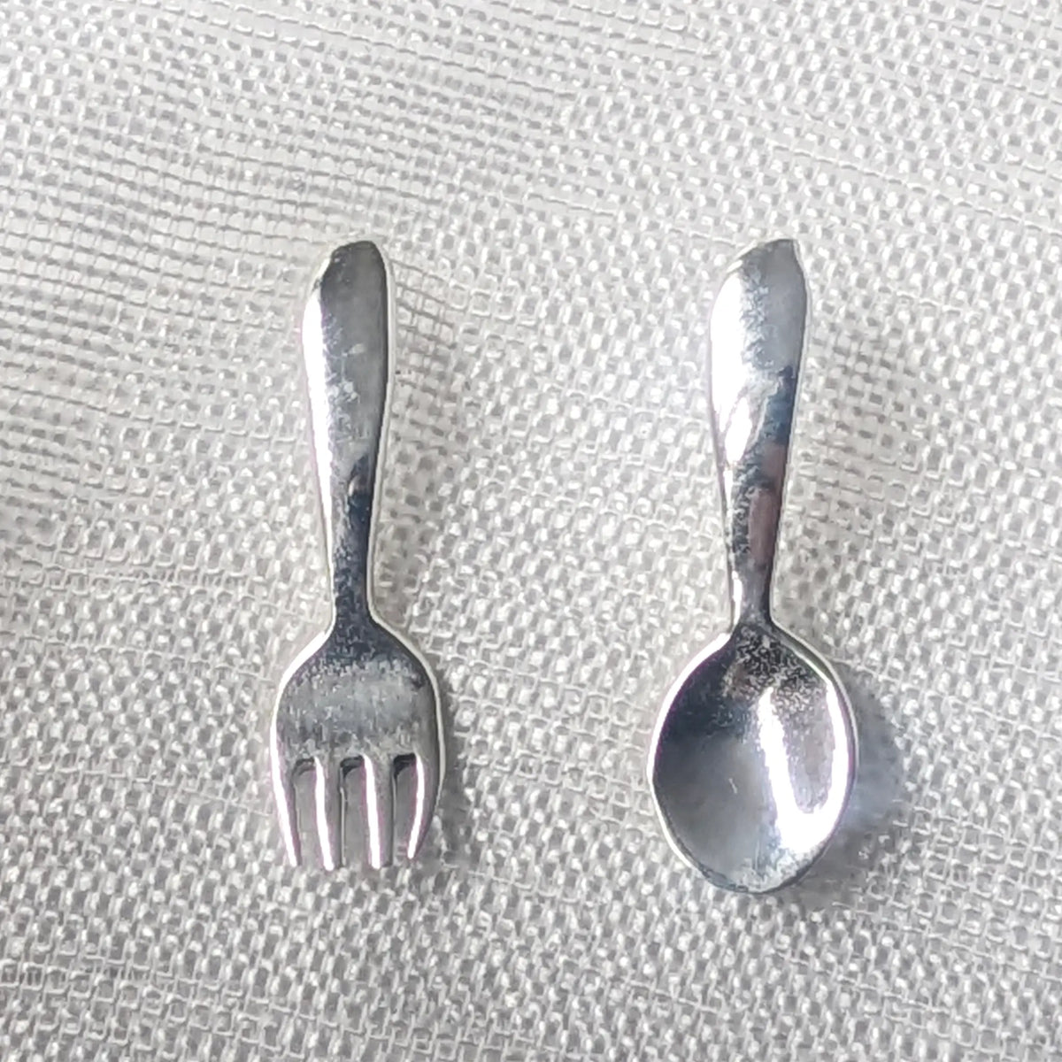 Detailaufnahme asymmetrische 925 Silber Ohrstecker im Gabel und Löffel Design auf hellem Stoff.