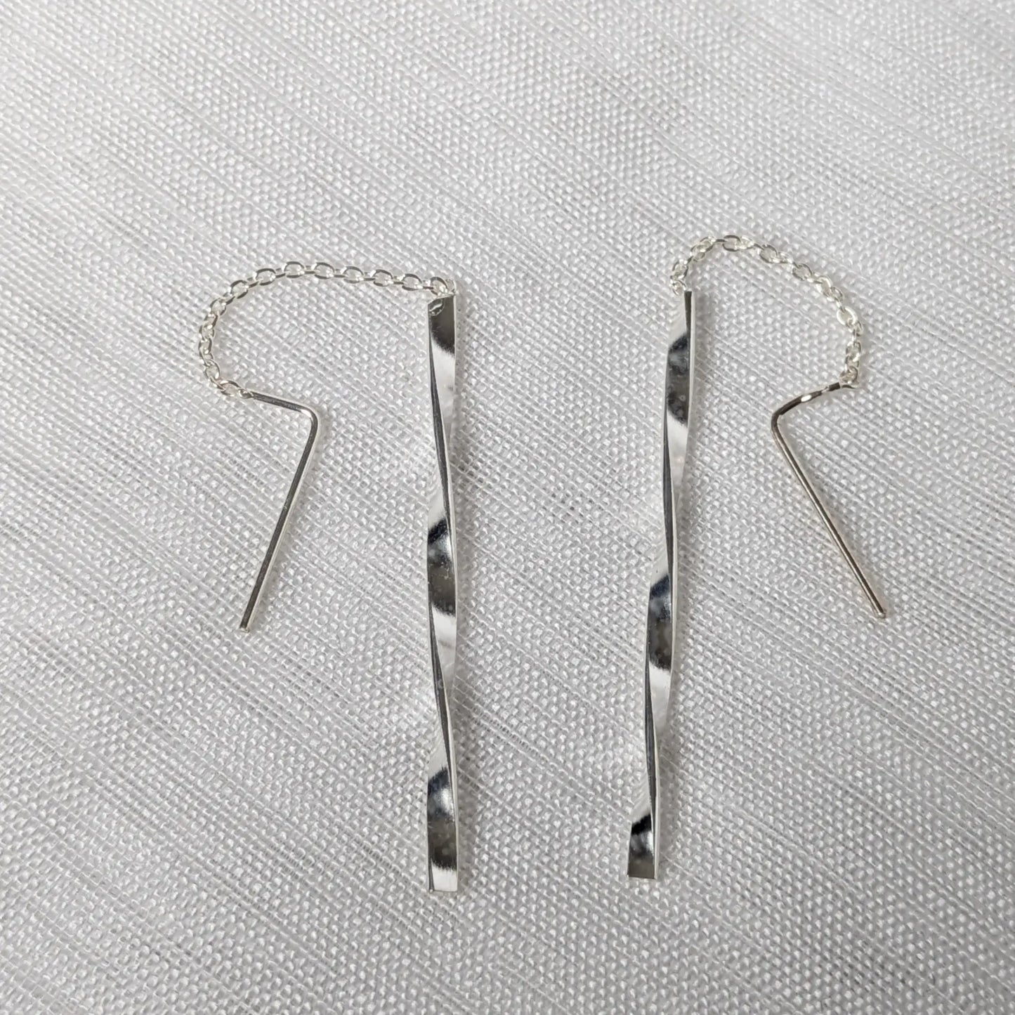 Nahaufnahme von zwei 925 Silber Durchzieher-Ohrringen mit feiner Kette und gedrehten, glänzenden Silberstäbchen im Wave-Design.