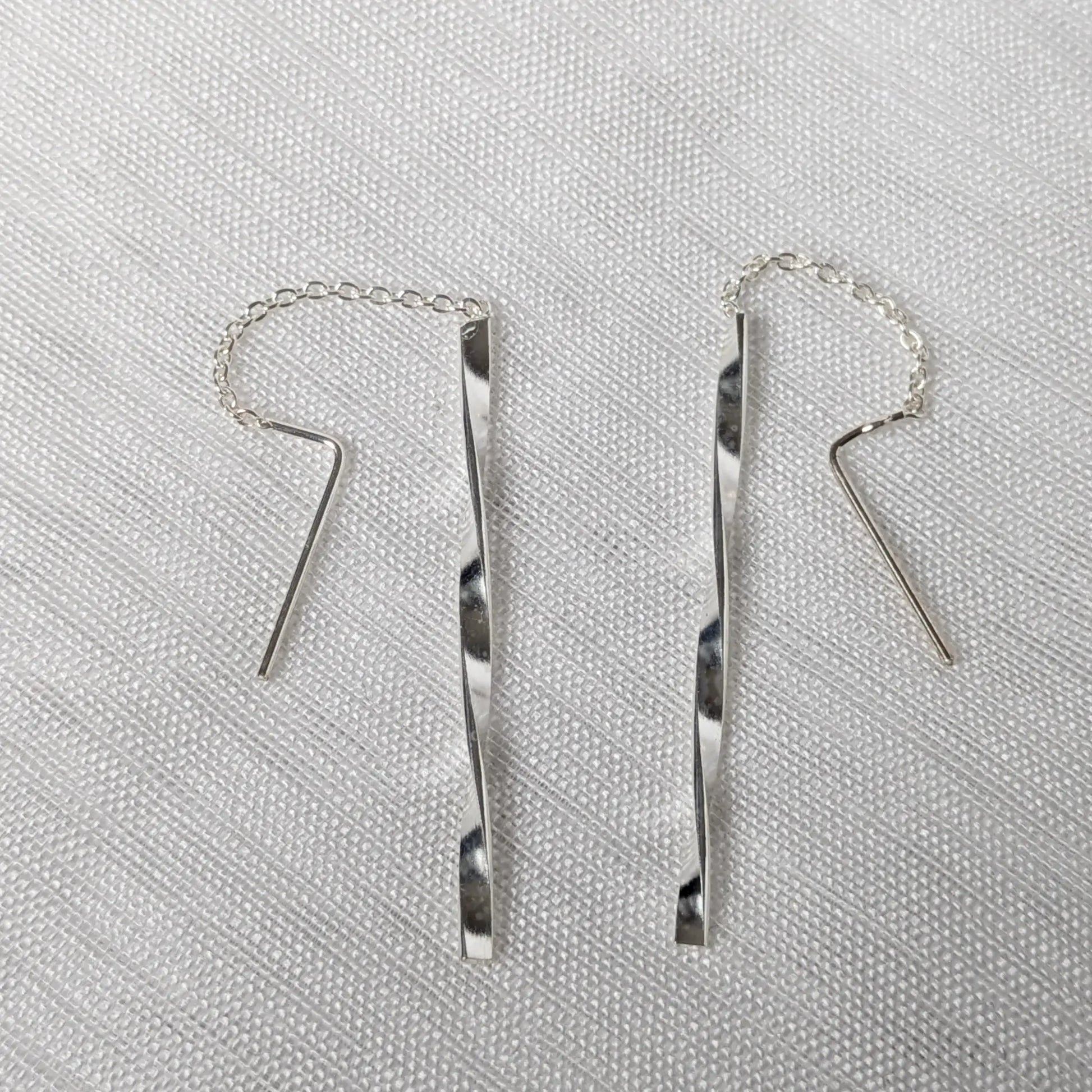 Nahaufnahme von zwei 925 Silber Durchzieher-Ohrringen mit feiner Kette und gedrehten, glänzenden Silberstäbchen im Wave-Design.