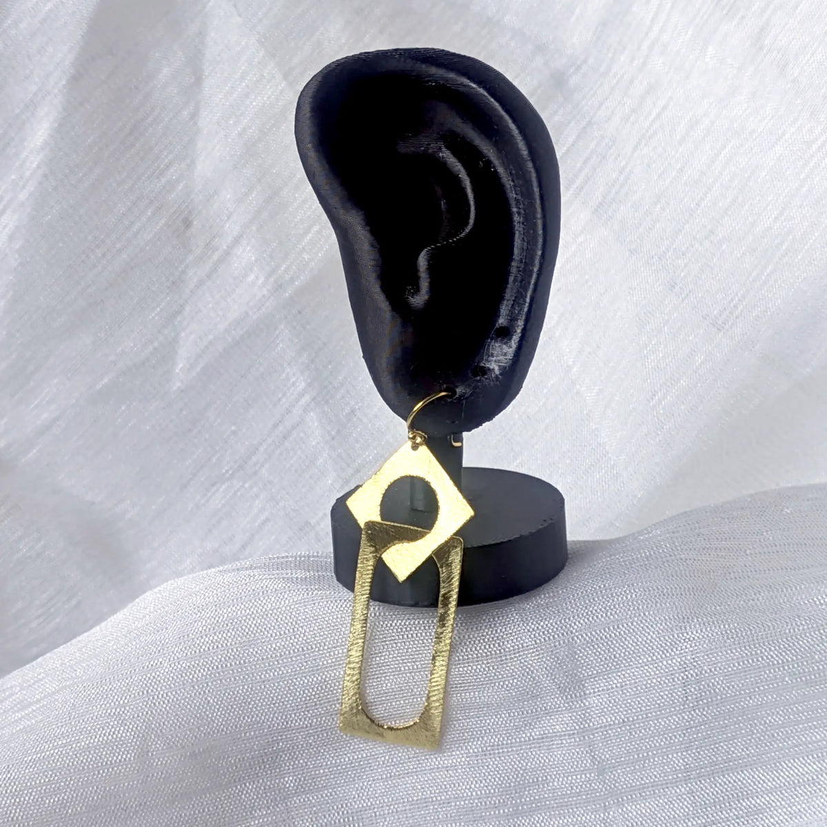 Geometrischer Statement-Ohrhänger in Gold getragen an einem schwarzen Ohr-Display zur Veranschaulichung der Länge