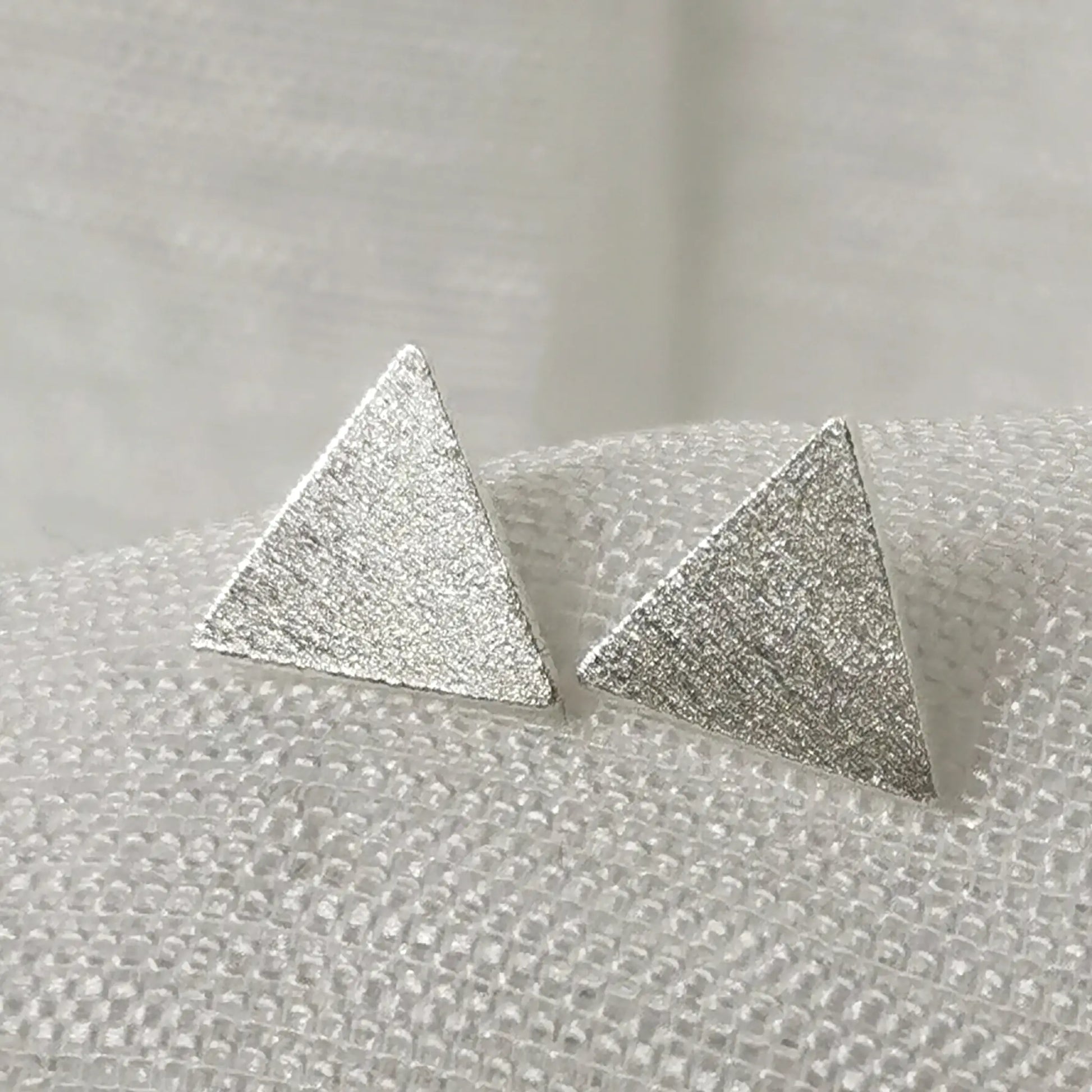 Nahaufnahme von geometrischen 925 Silber Ohrsteckern in Dreieck-Form mit detailreich gebürsteter, mattierter Oberfläche