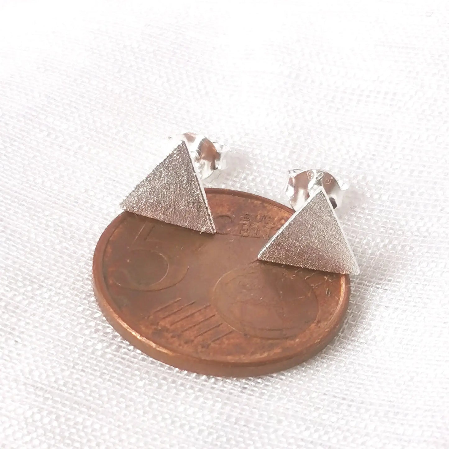 Größenvergleich: Das geometrische Silber-Ohrstecker-Dreieck platziert auf einer 5-Cent-Münze zur exakten Einschätzung der Maße.