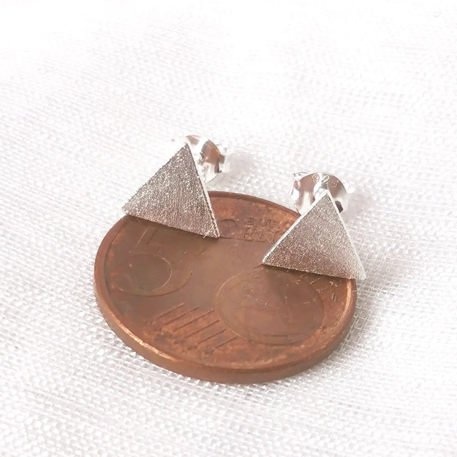 Größenvergleich: Das geometrische Silber-Ohrstecker-Dreieck platziert auf einer 5-Cent-Münze zur exakten Einschätzung der Maße.