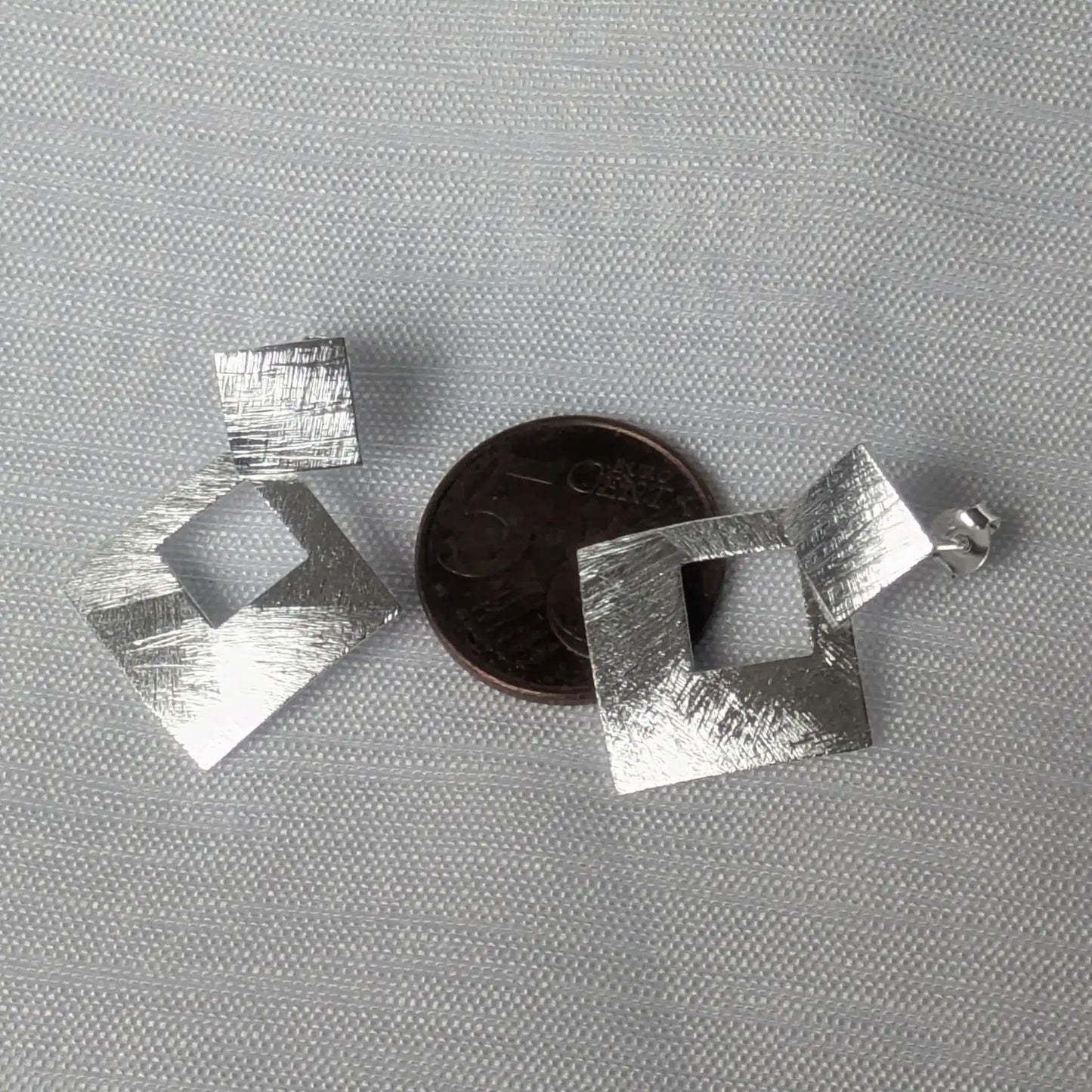 Quadratische Silberstecker im Größenvergleich auf einer 5-Cent-Münze.