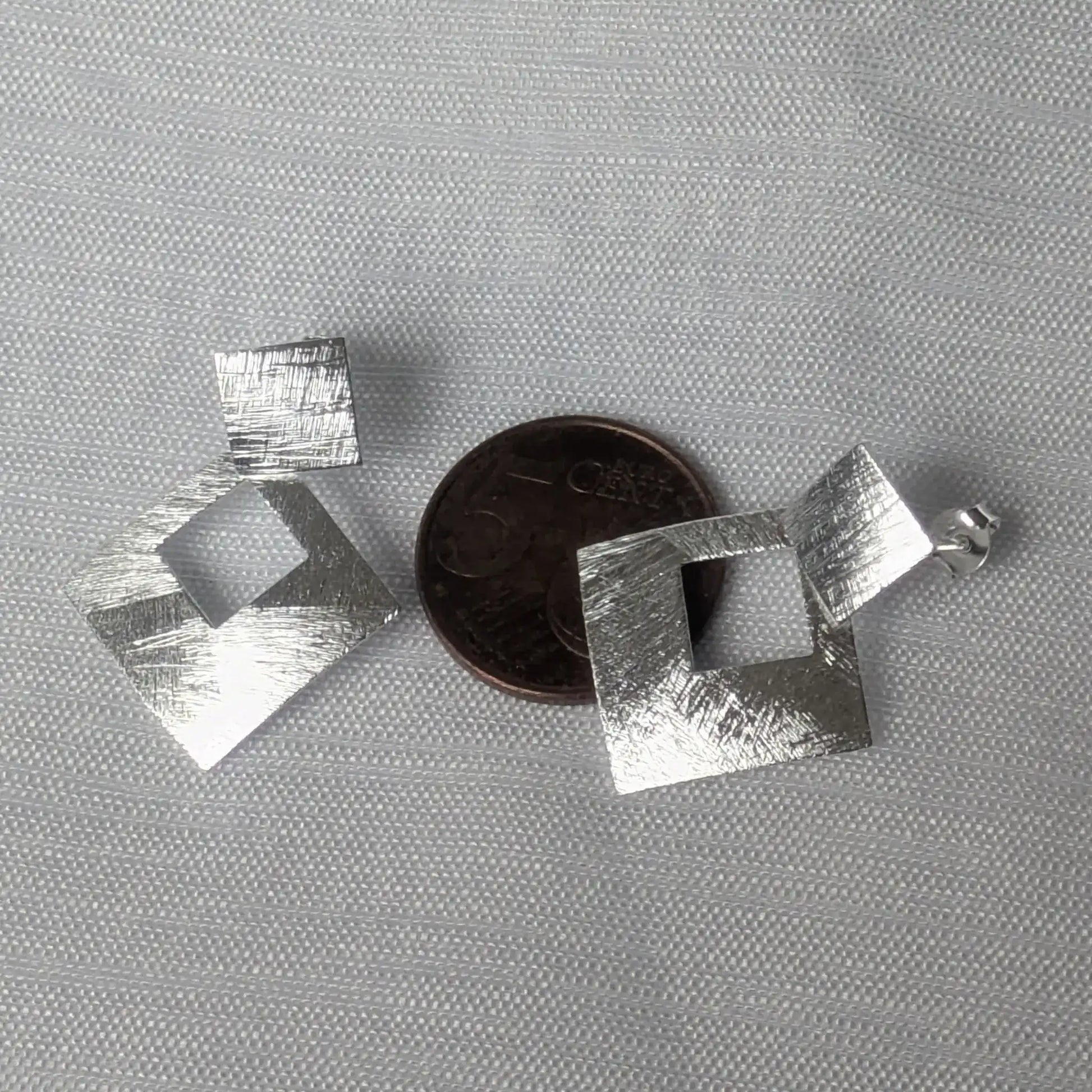 Quadratische Silberstecker im Größenvergleich auf einer 5-Cent-Münze.