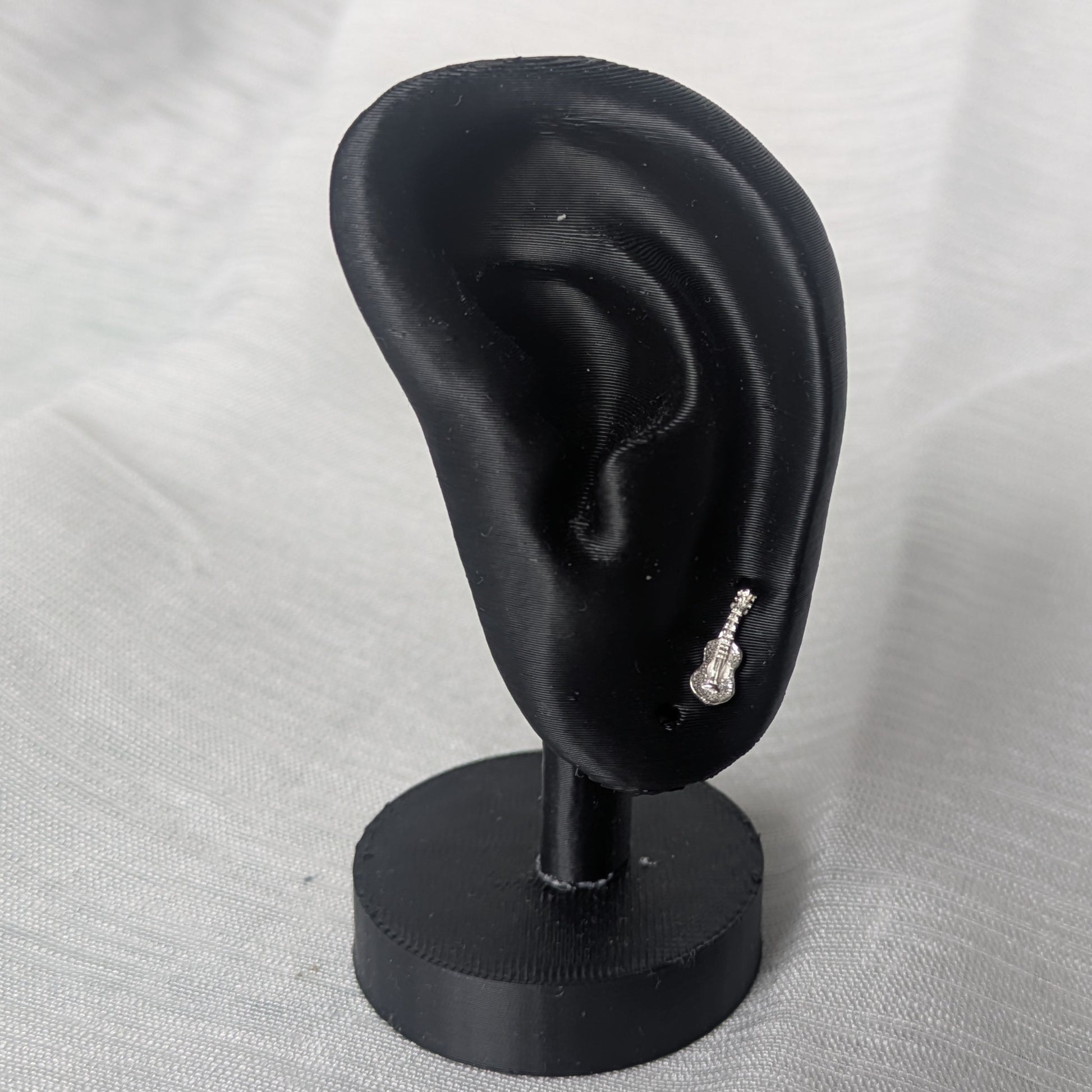 Miniatur-Gitarren Ohrstecker an einem schwarzen Ohrdisplay zur Darstellung der Proportionen und der eleganten Wirkung am Ohr.
