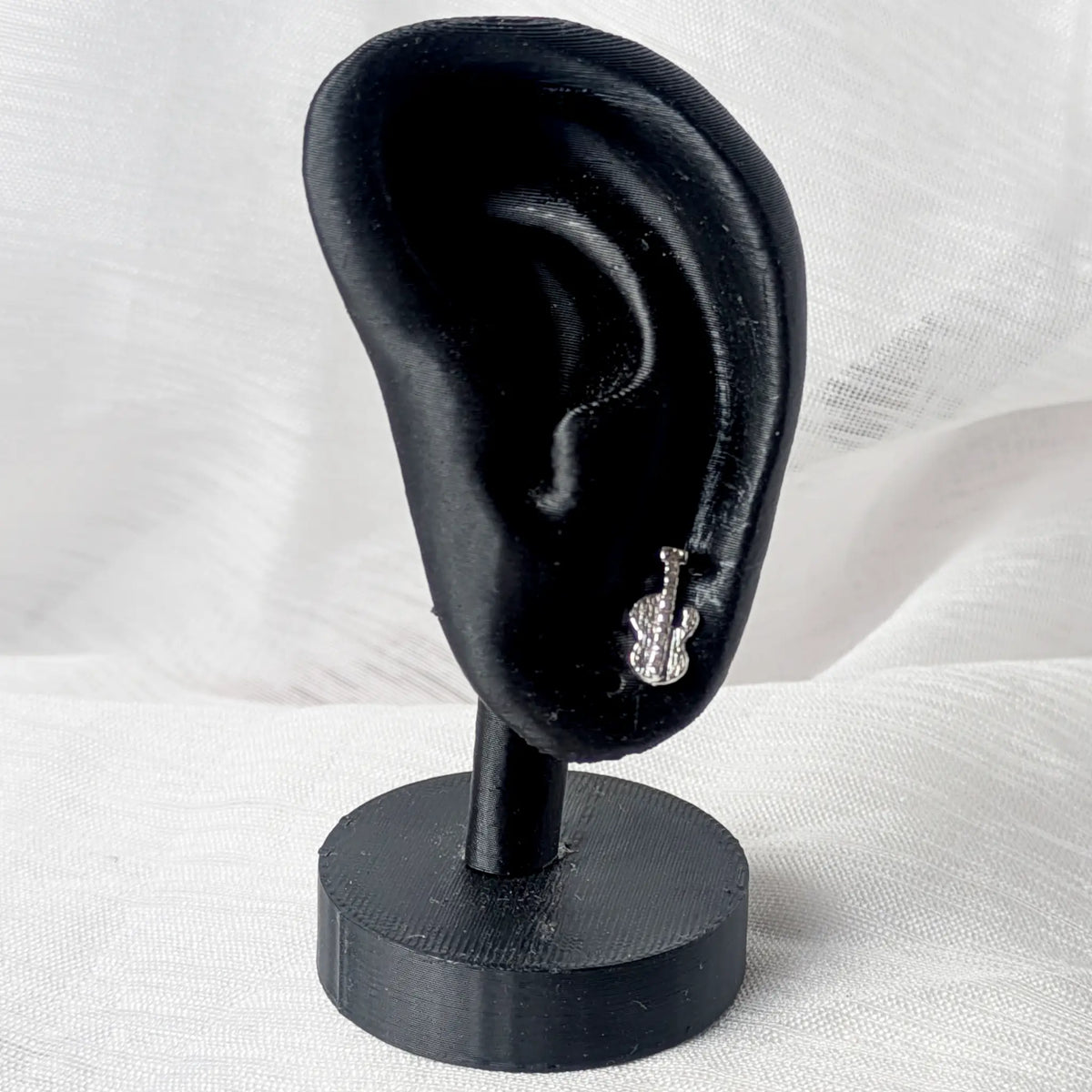 Ein silberner E-Gitarren-Ohrstecker, getragen am Ohrläppchen eines schwarzen 3D-Modell-Ohrs zur Größenveranschaulichung.