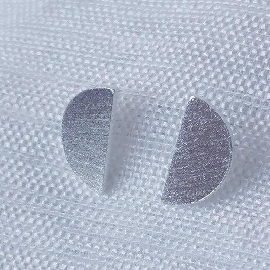 Nahaufnahme von zwei minimalistischen Halbkreis-Ohrsteckern aus 925 Silber mit einer fein gebürsteten, mattierten Oberfläche.