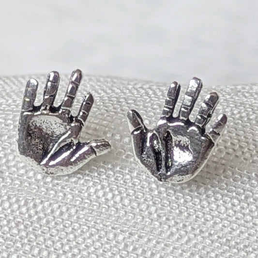 `Nahaufnahme von zwei detailreichen Ohrsteckern in Hand-Form aus geschwärztem 925 Sterlingsilber auf strukturiertem Stoff.
