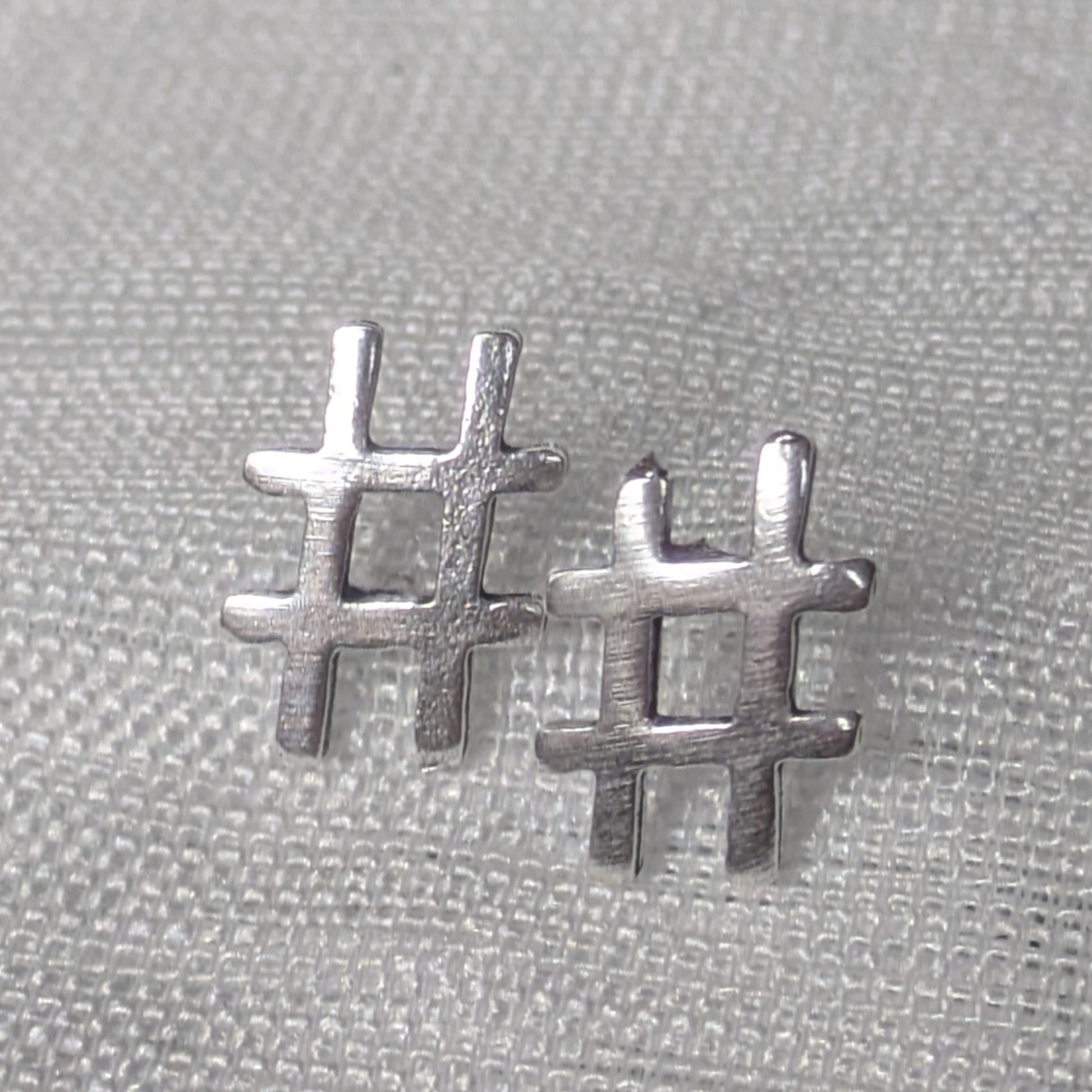 Frontalansicht der silbernen Hashtag-Ohrstecker mit mattierter Oberfläche auf hellem Stoff