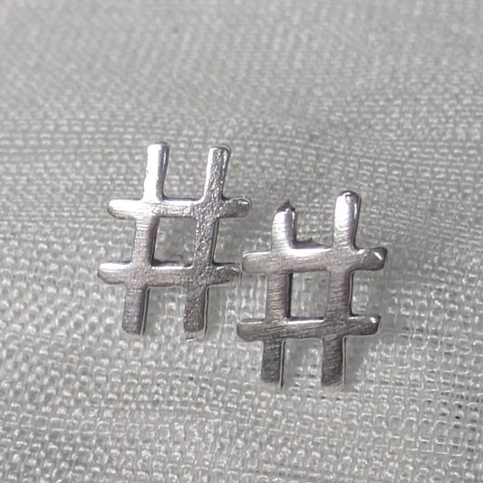 Frontalansicht der silbernen Hashtag-Ohrstecker mit mattierter Oberfläche auf hellem Stoff