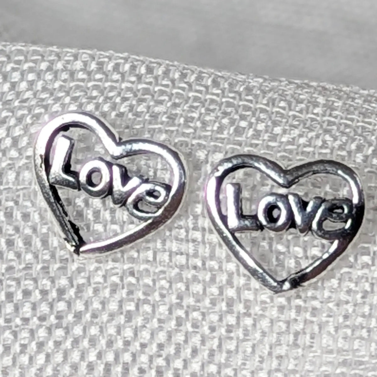 Nahaufnahme der 925 Silber Ohrstecker in Herzform mit integriertem Love-Schriftzug