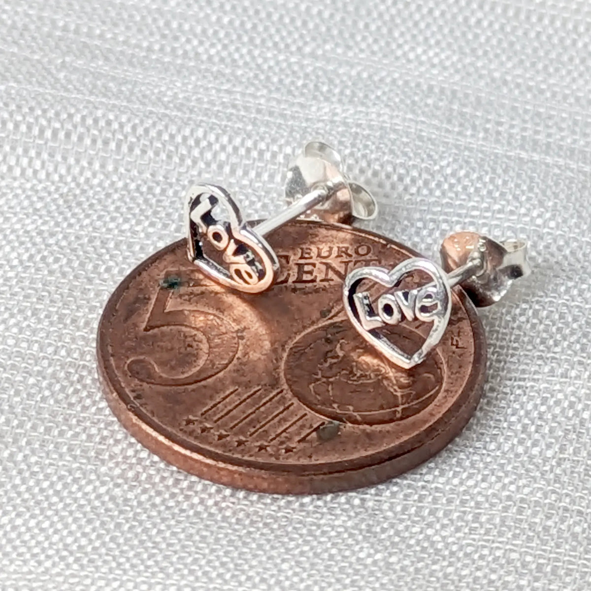 Größenvergleich: Filigrane 925 Silber Love Ohrstecker flach platziert auf einer 5-Cent-Münze.