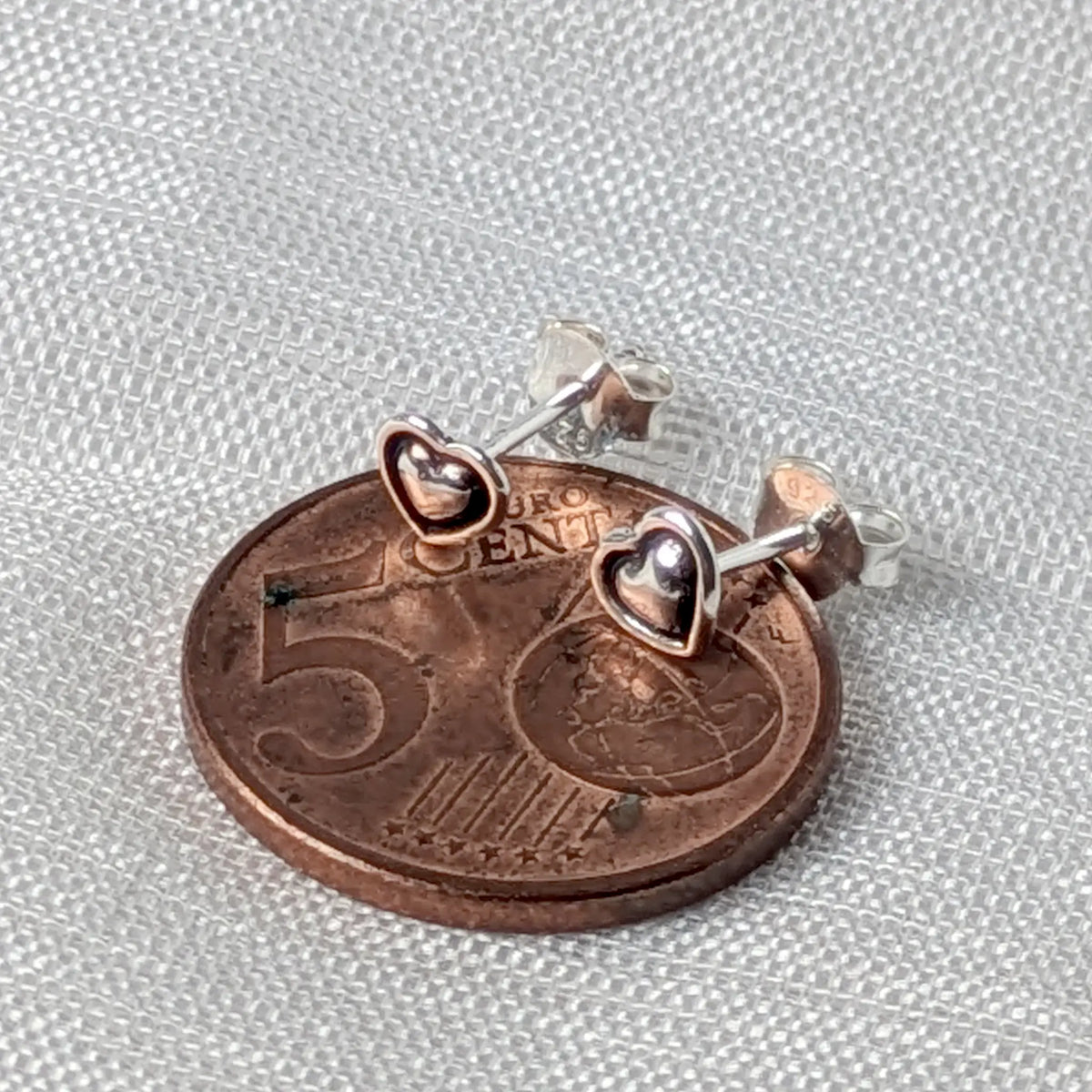 Größenvergleich: Die filigranen 925 Silber Herz-Ohrstecker flach liegend auf einer 5-Cent-Münze.